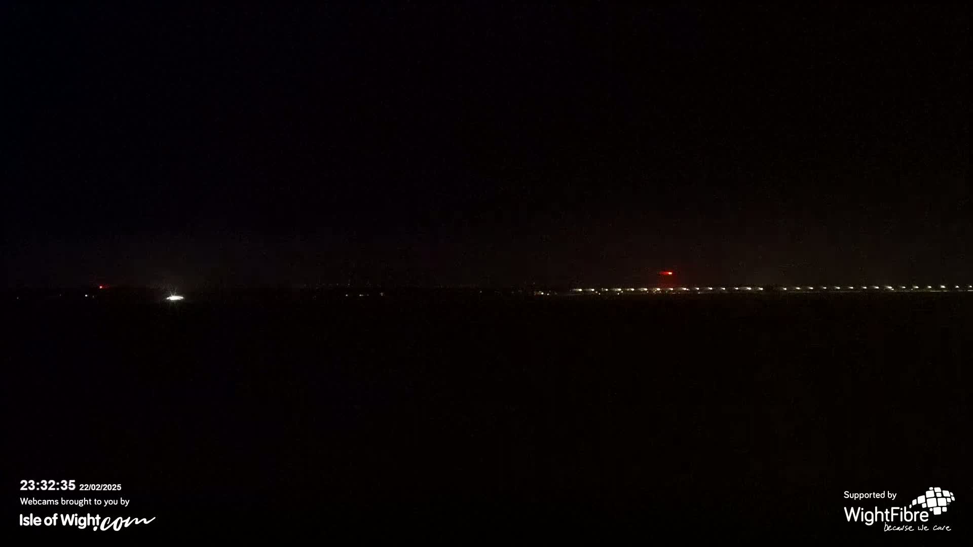 A dark nighttime scene shows a distant line of lights on the horizon.
