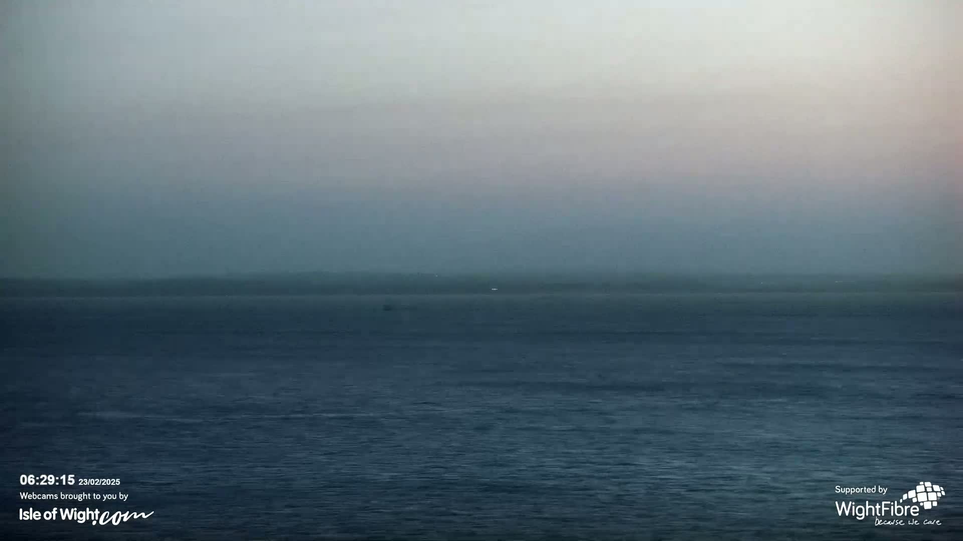 A hazy, dark-blue sea stretches to a barely visible, hazy shoreline under a muted sky.