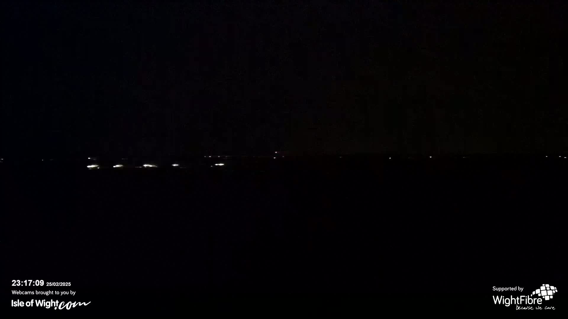 A dark nighttime scene shows a distant line of faint lights on the horizon.