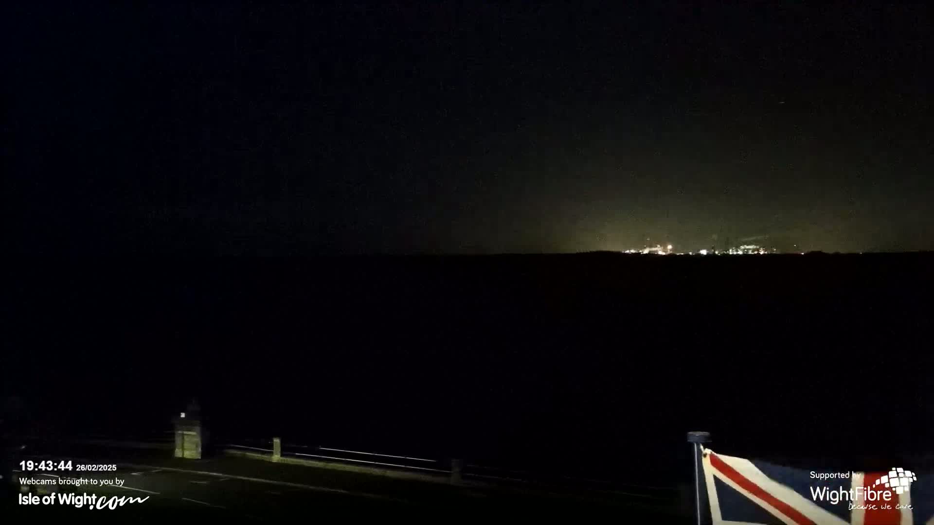 A nighttime view of a dark landscape with faintly visible lights on the horizon under a clear, dark sky.