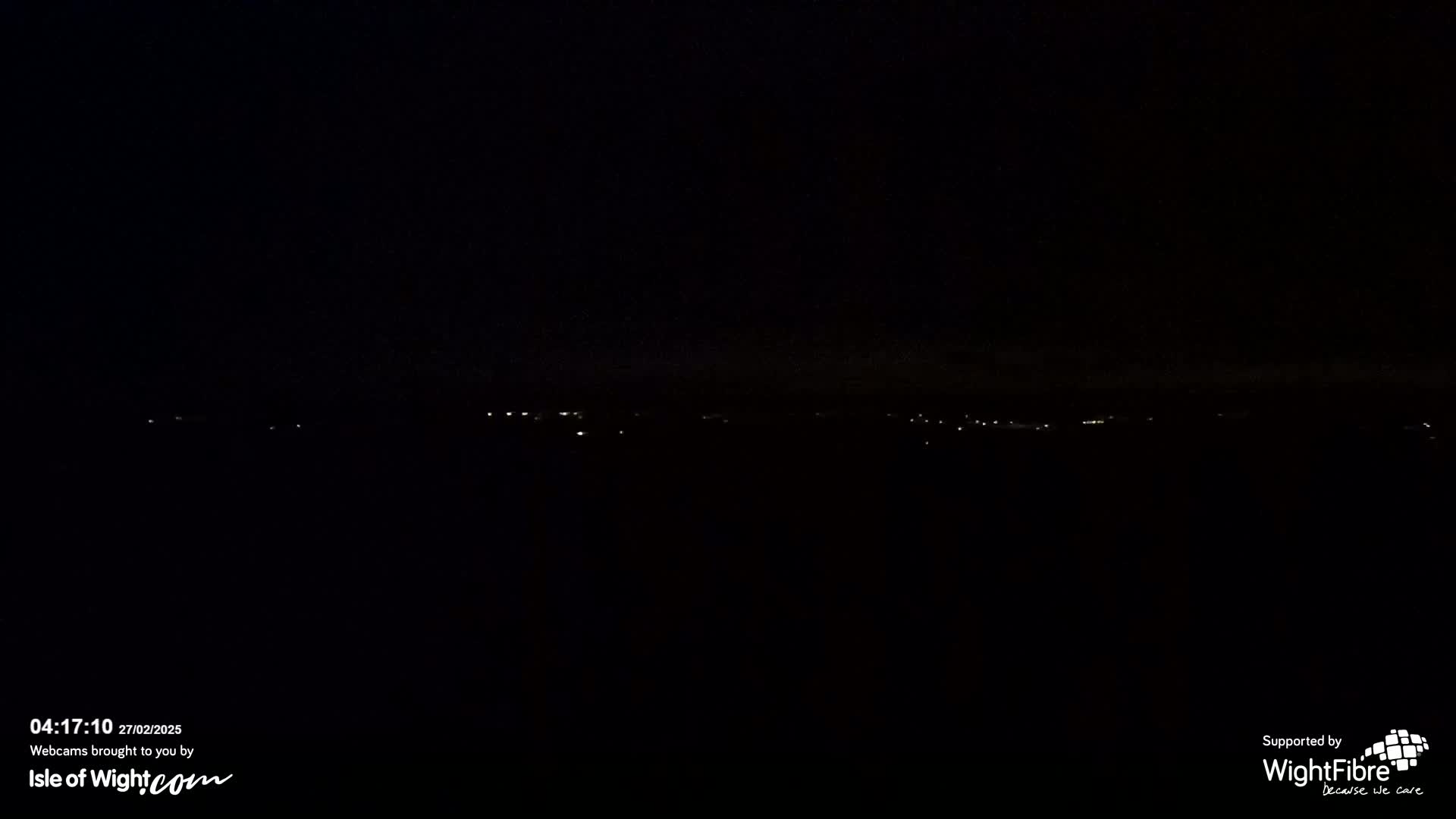 A dark, nighttime landscape shows a distant line of faint lights.
