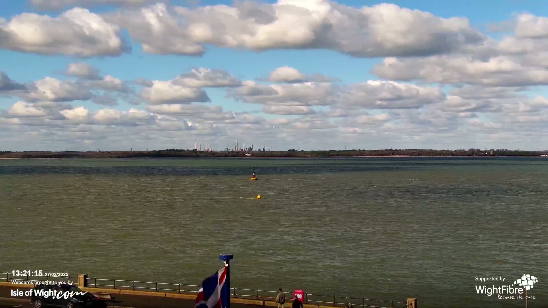 A partly cloudy day shows a wide expanse of calm, greenish-gray water with a distant industrial horizon.