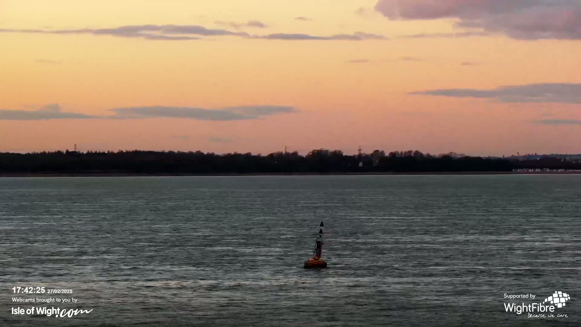 A body of water with a small orange buoy in the center, under a pale pink and orange sunset sky.