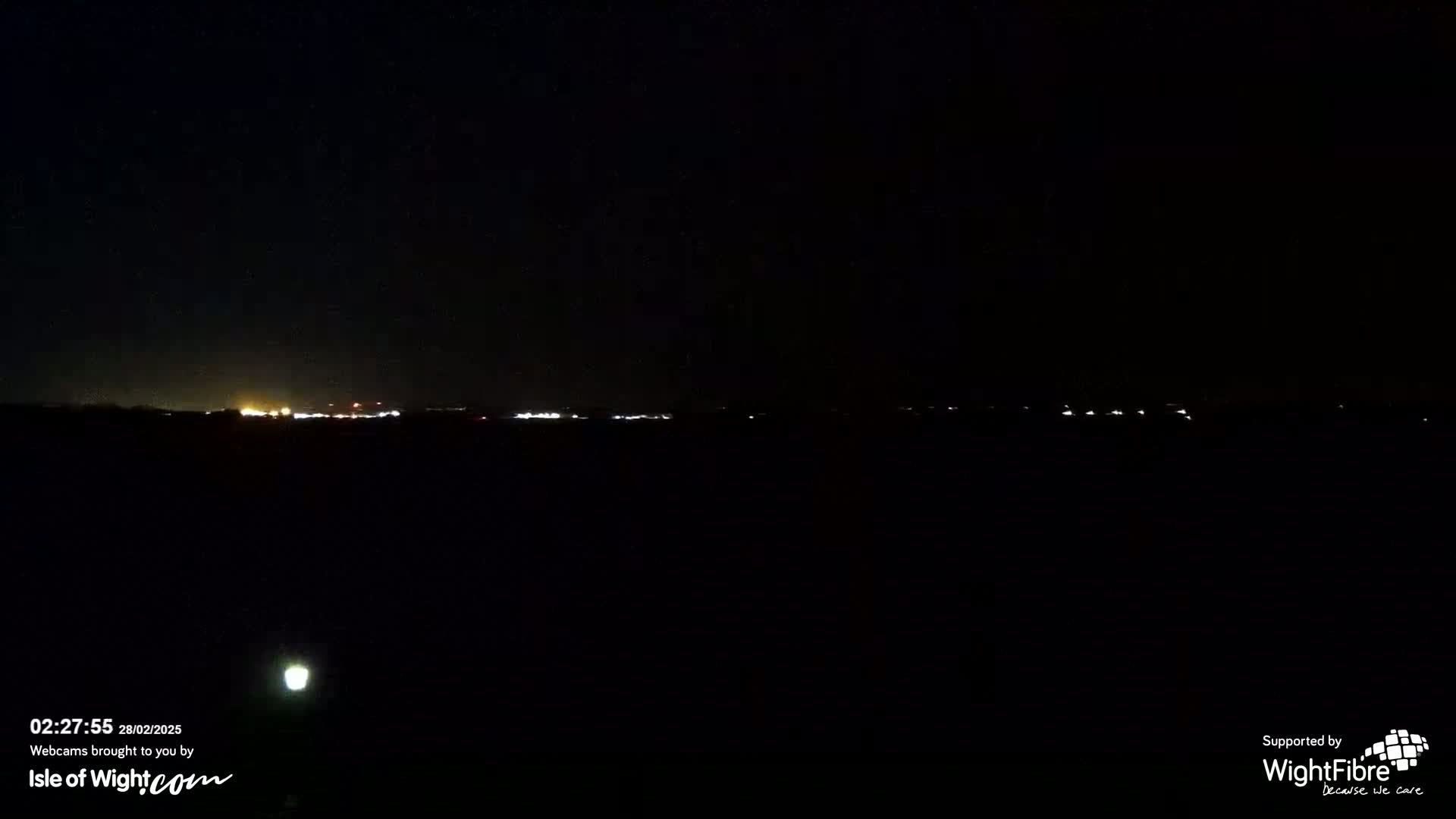 A dark, nighttime scene shows a distant line of lights on the horizon.