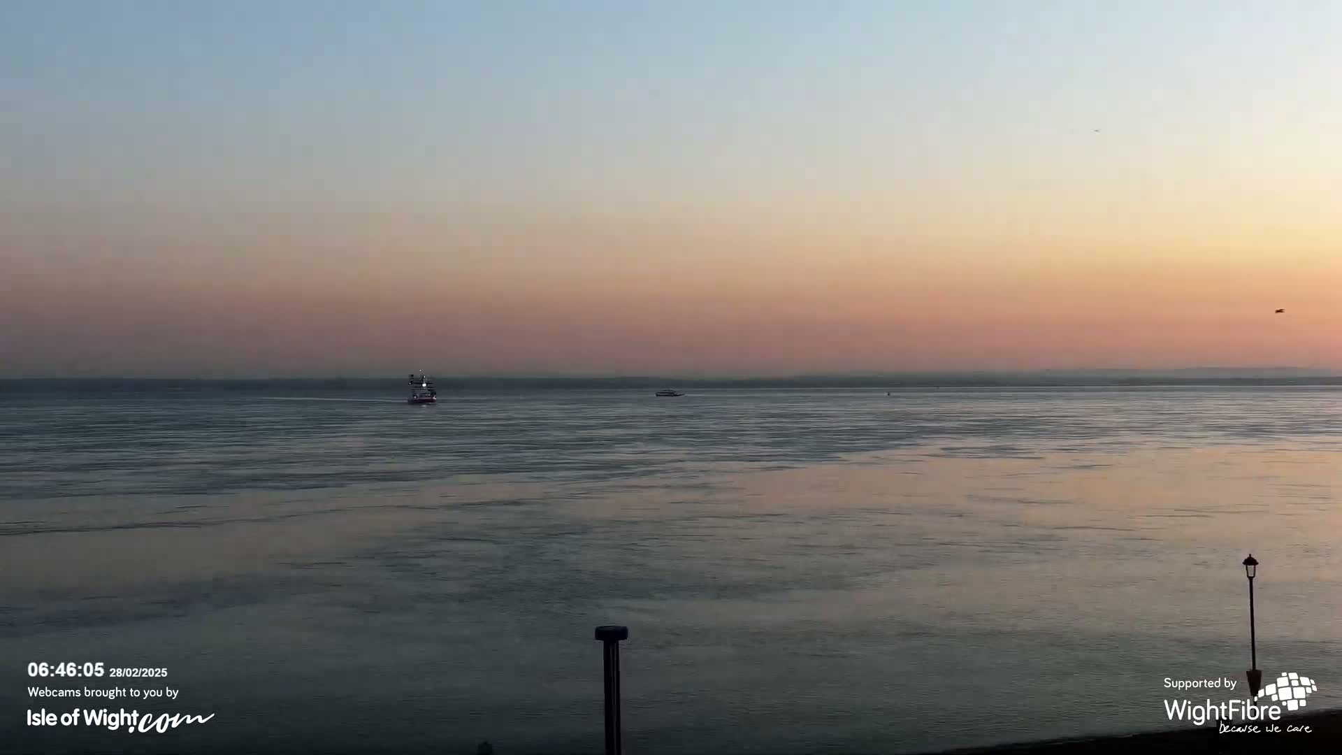 A calm body of water at sunset with a few small boats visible on the horizon.
