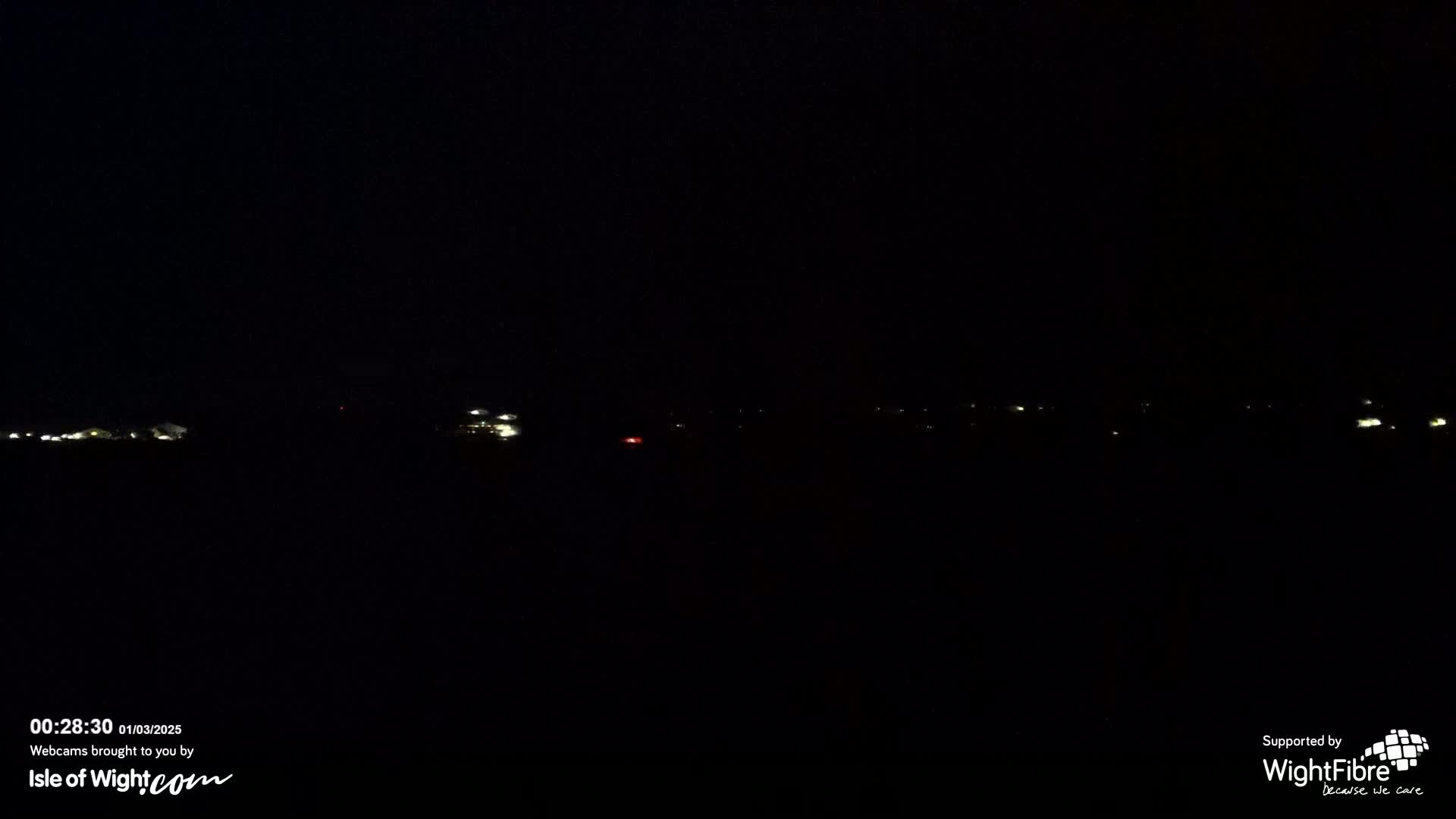 A nighttime long shot of faintly lit buildings and possibly cars in the distance under a dark sky.
