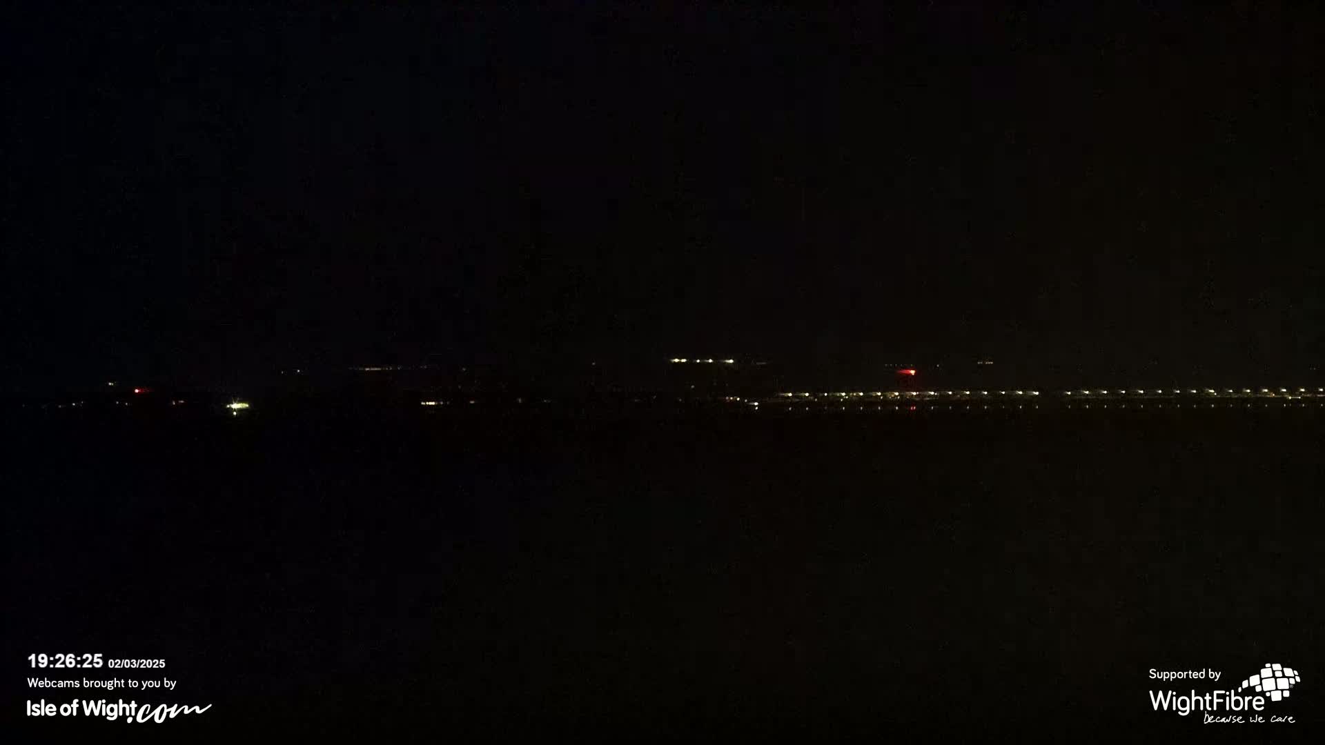 A dark nighttime scene shows a distant line of lights across a body of water.