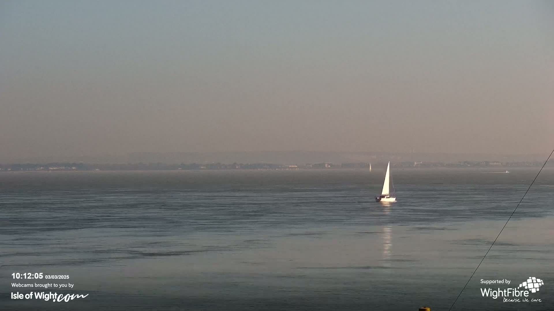 A sailboat is visible on a hazy, calm body of water with a distant shoreline.
