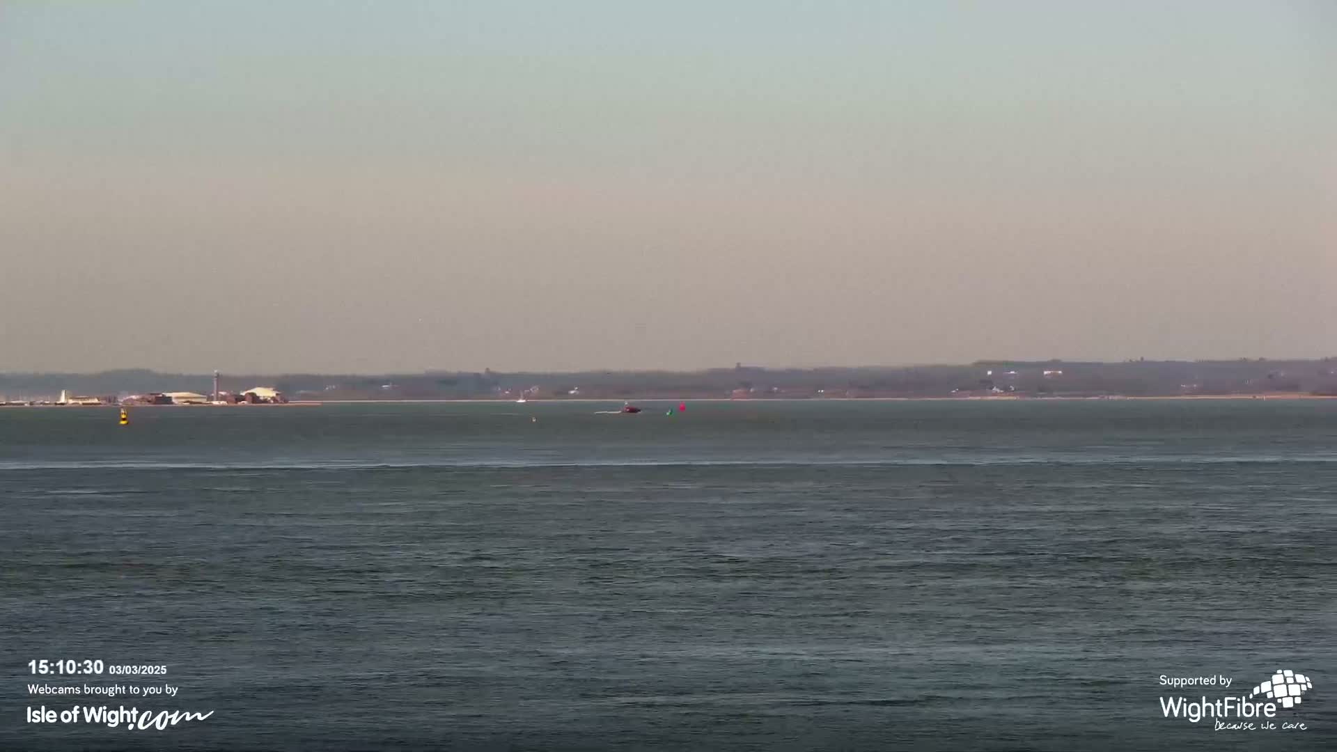A calm body of water shows a distant shoreline under a hazy sky.