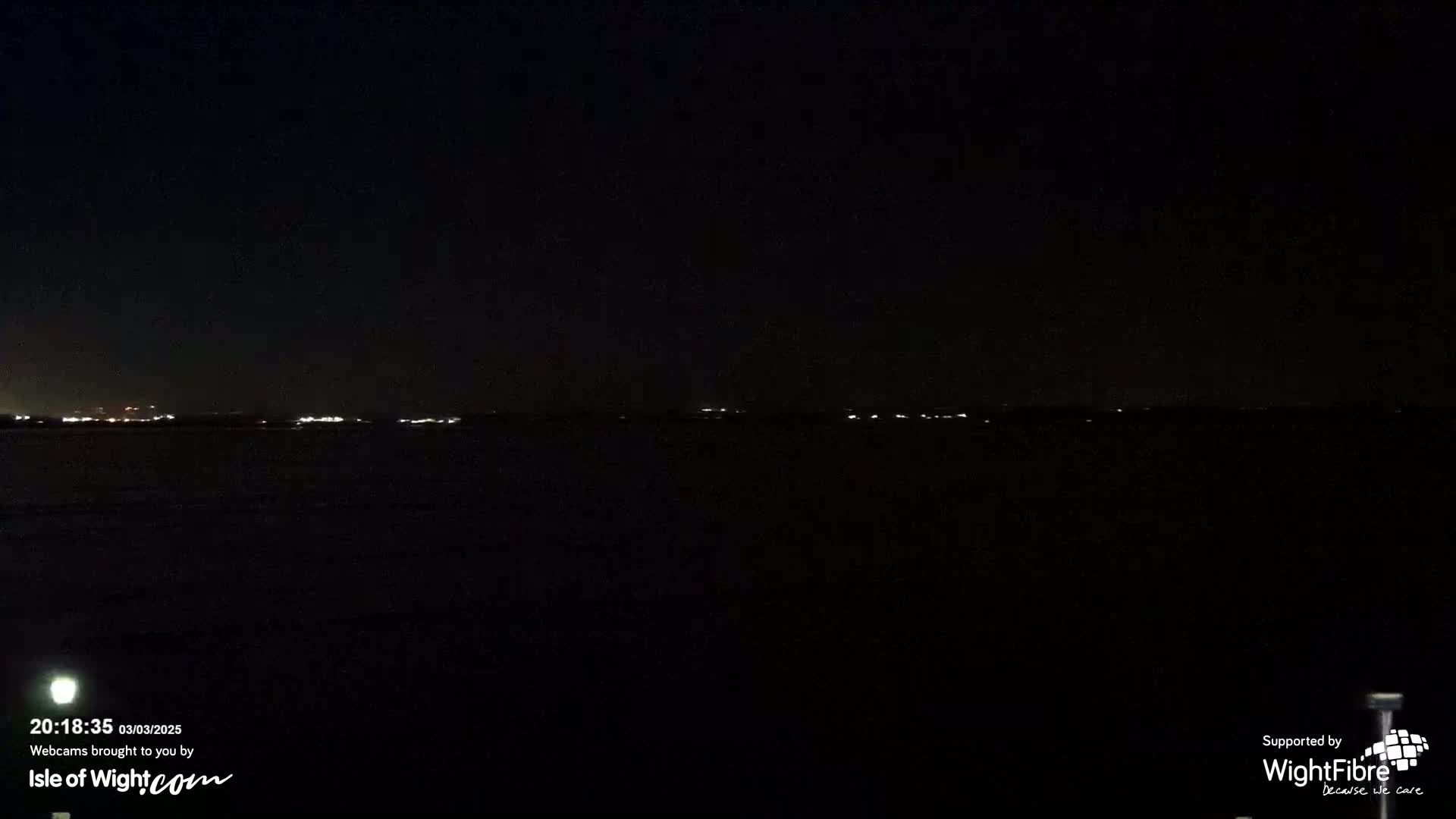 A dark, nighttime view of a body of water with a distant, faintly lit shoreline.