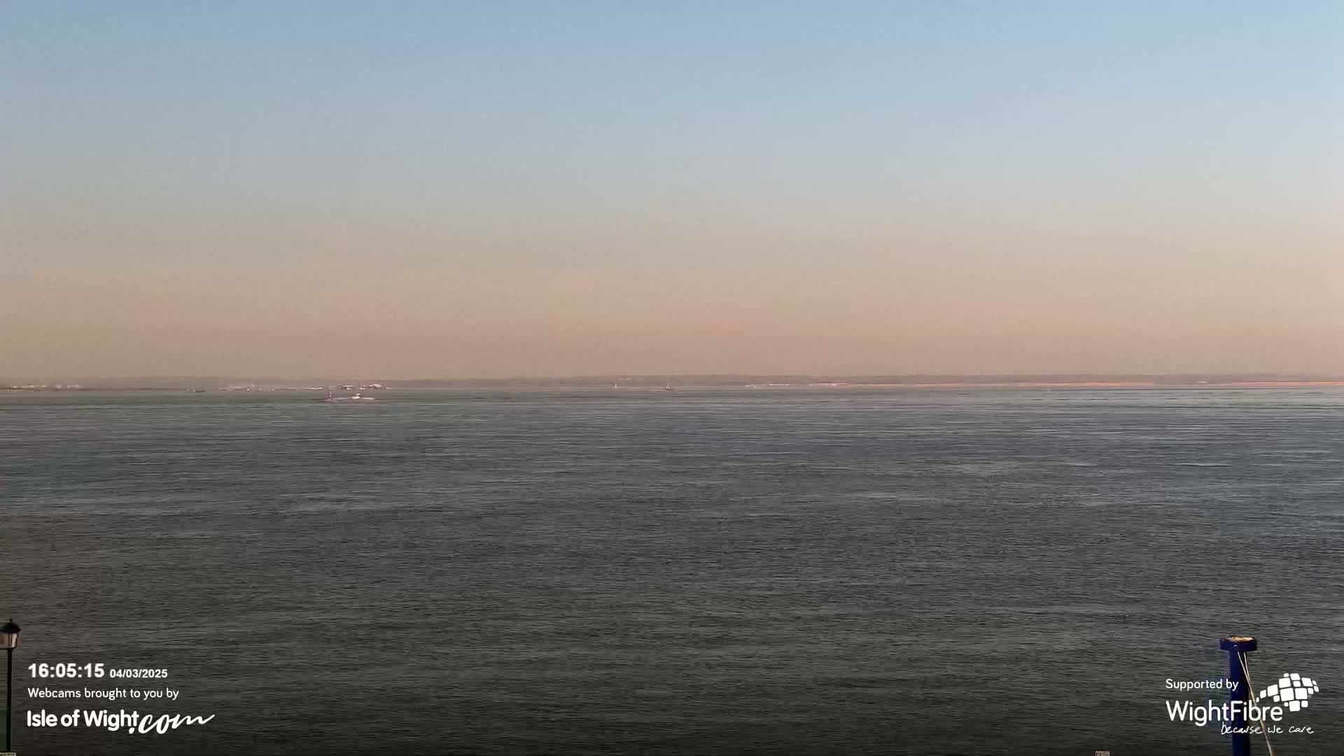 A calm, hazy body of water stretches to a distant shoreline under a pale blue sky.