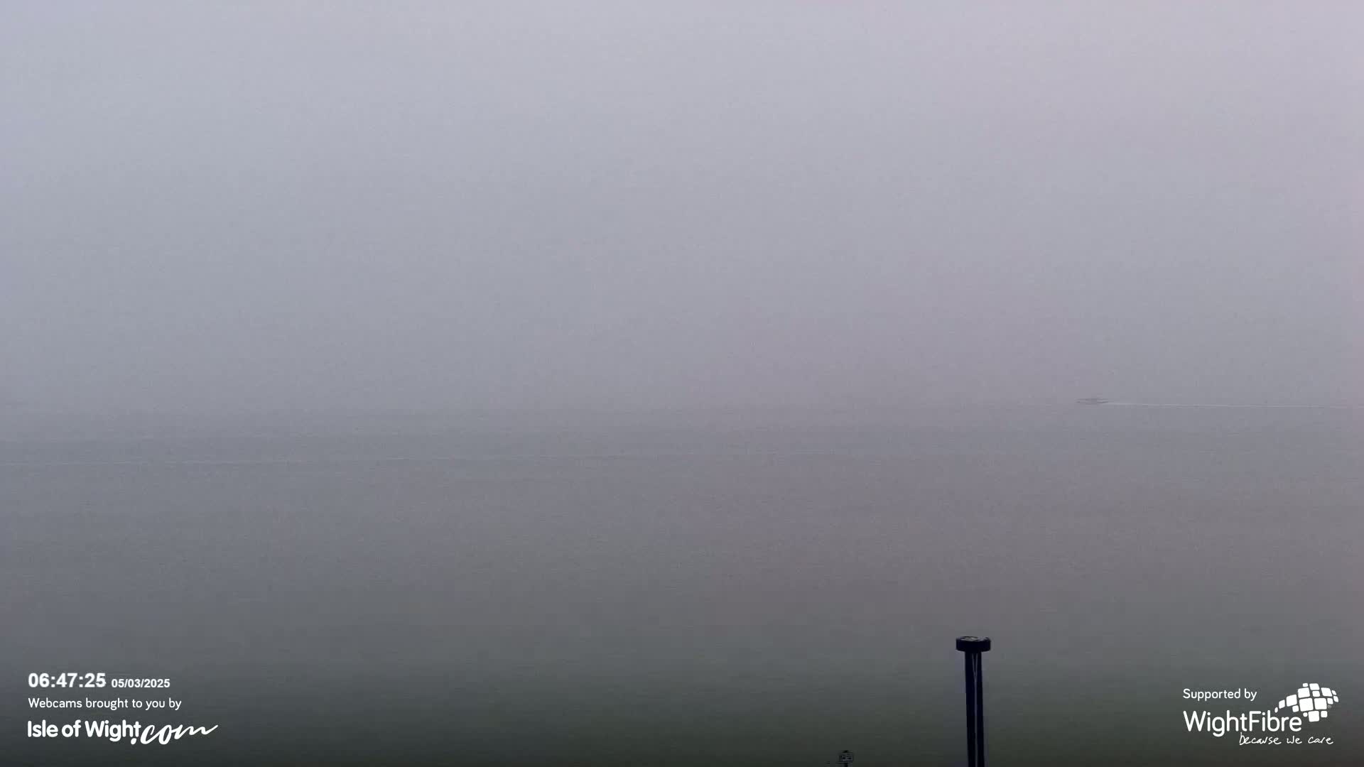 A distant, small boat is barely visible on a foggy body of water.