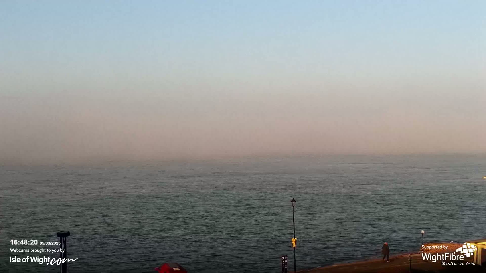 A hazy, calm sea stretches to a pale, muted sky under a light fog.