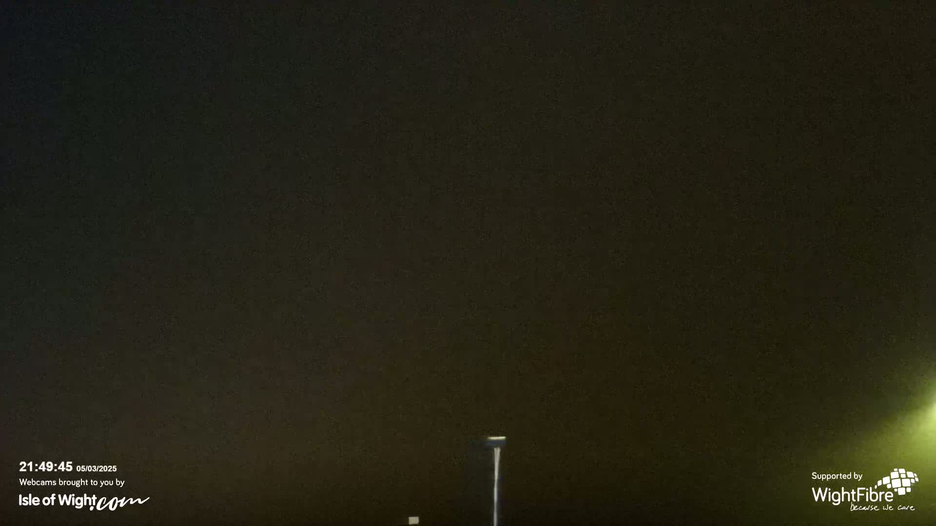 A dark, nighttime scene shows a single lamppost under a hazy, dark sky.