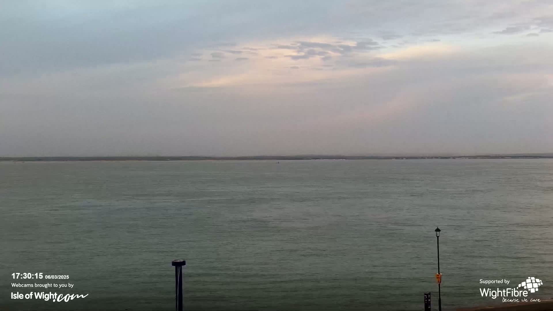 A calm, overcast day shows a wide expanse of water stretching to a distant shoreline.