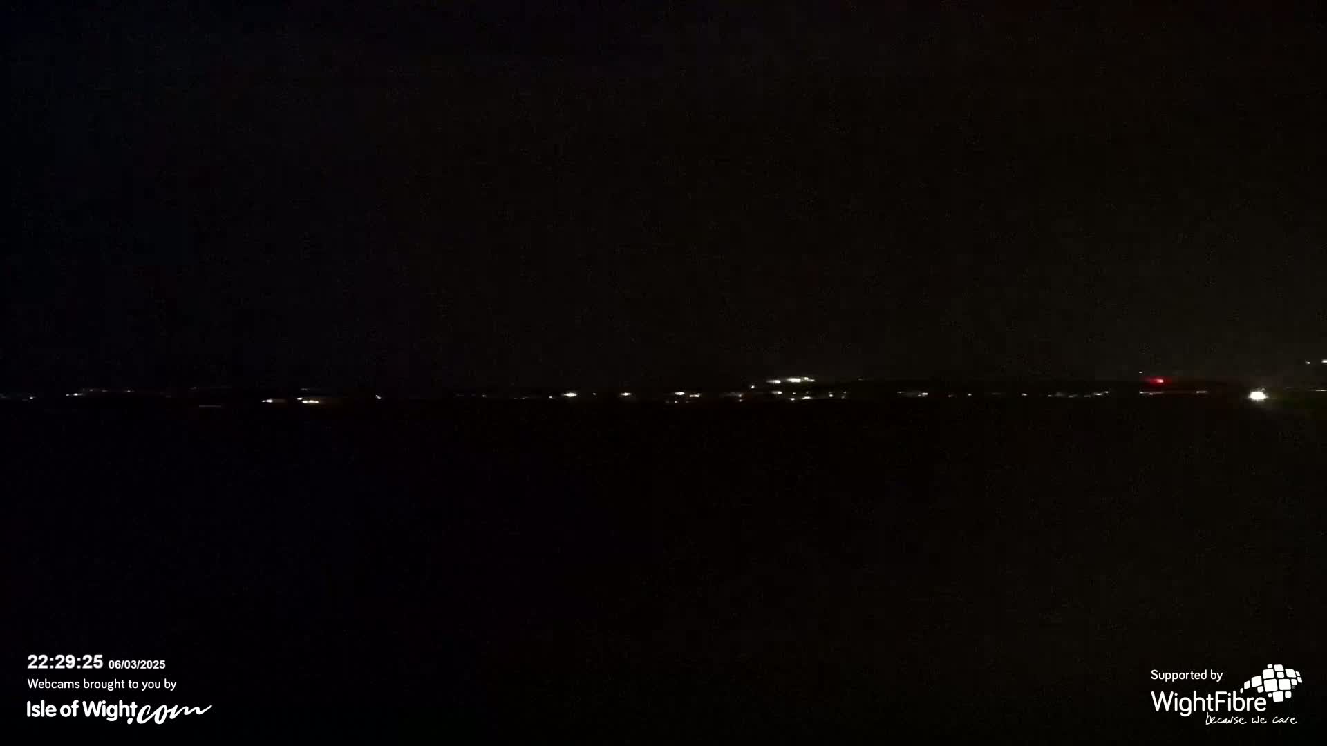 A dark nighttime scene shows a distant line of faint lights on a horizon.