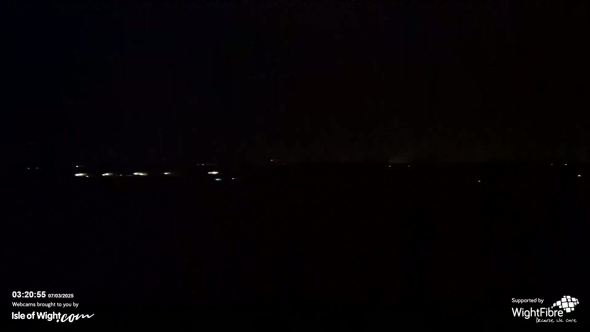 A dark nighttime scene shows a distant line of faint lights on a dark horizon.