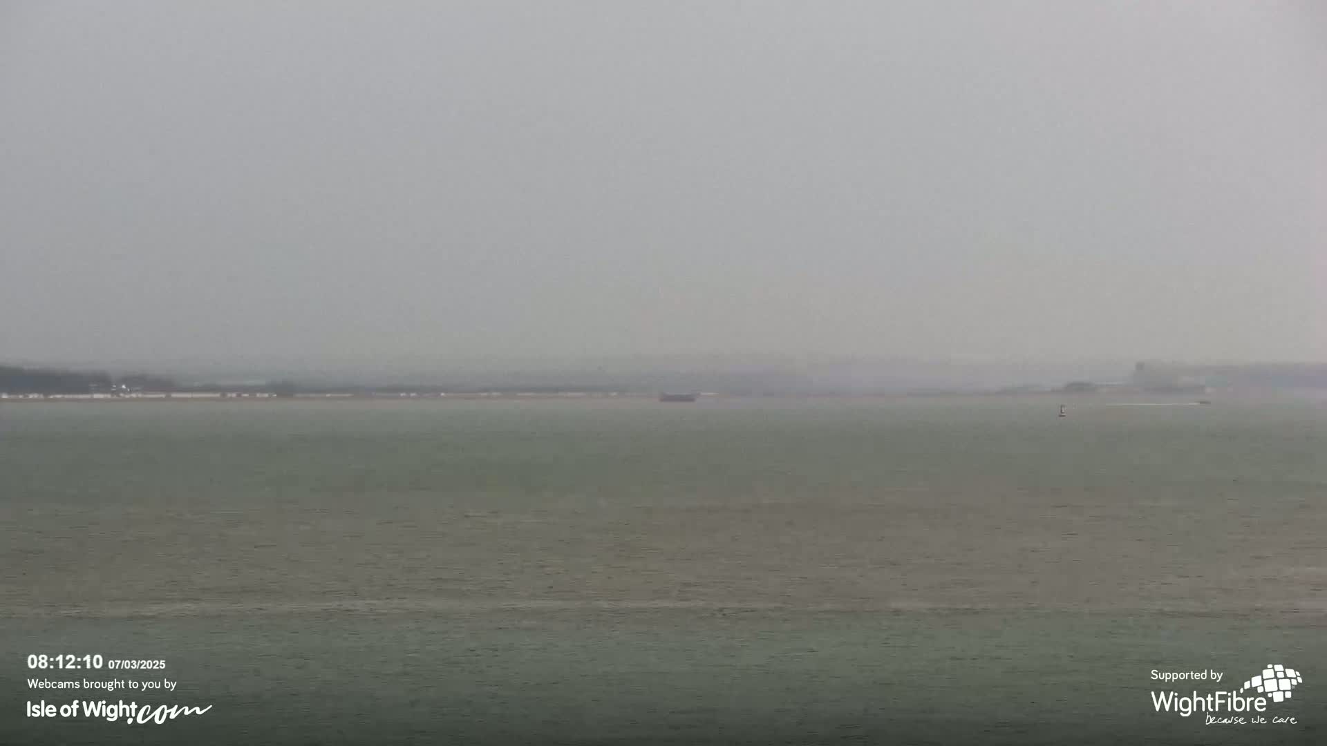 A calm body of water stretches to a hazy, distant shoreline under an overcast sky.