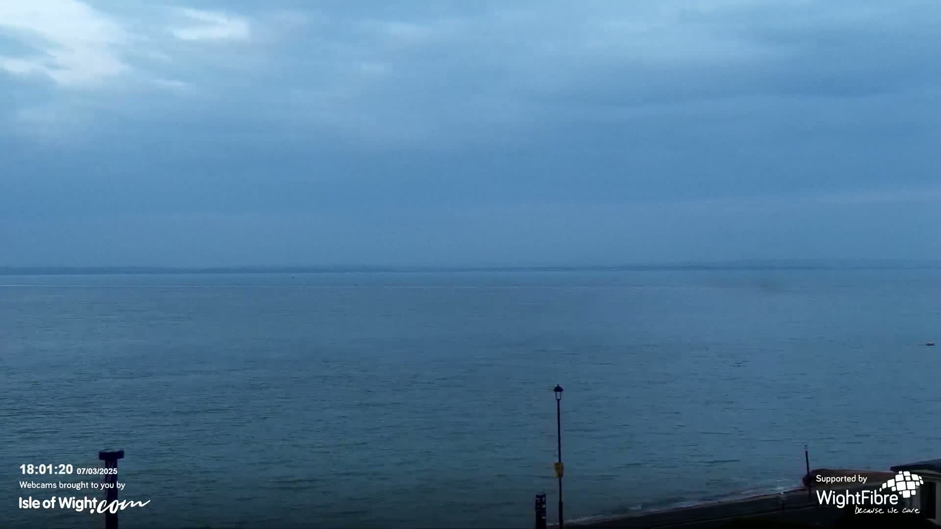 A calm, dark blue sea stretches to a hazy horizon under a cloudy sky.