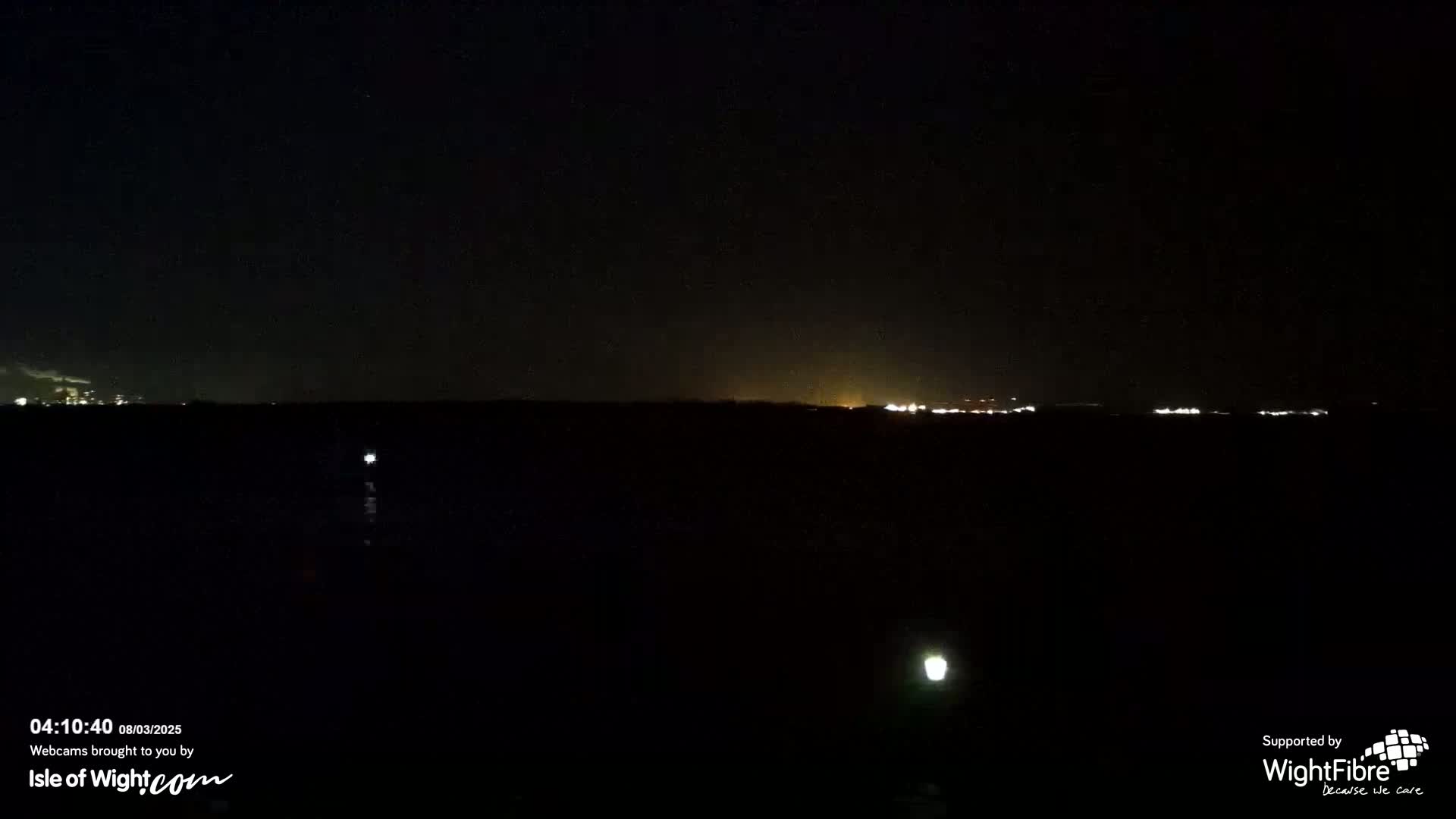 A dark, nighttime scene shows a distant line of lights on the horizon over a mostly black body of water or land.