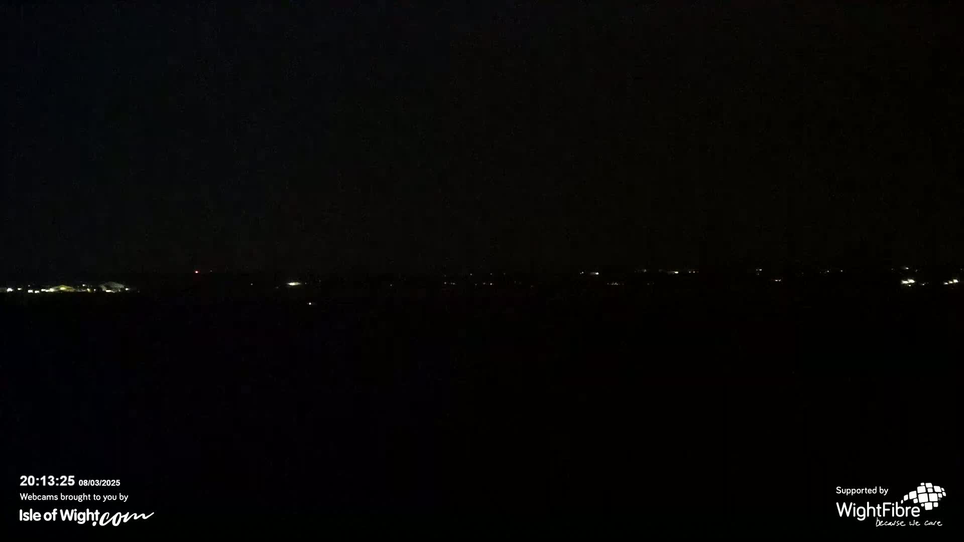 A dark, nighttime landscape shows a distant line of faint lights on the horizon.