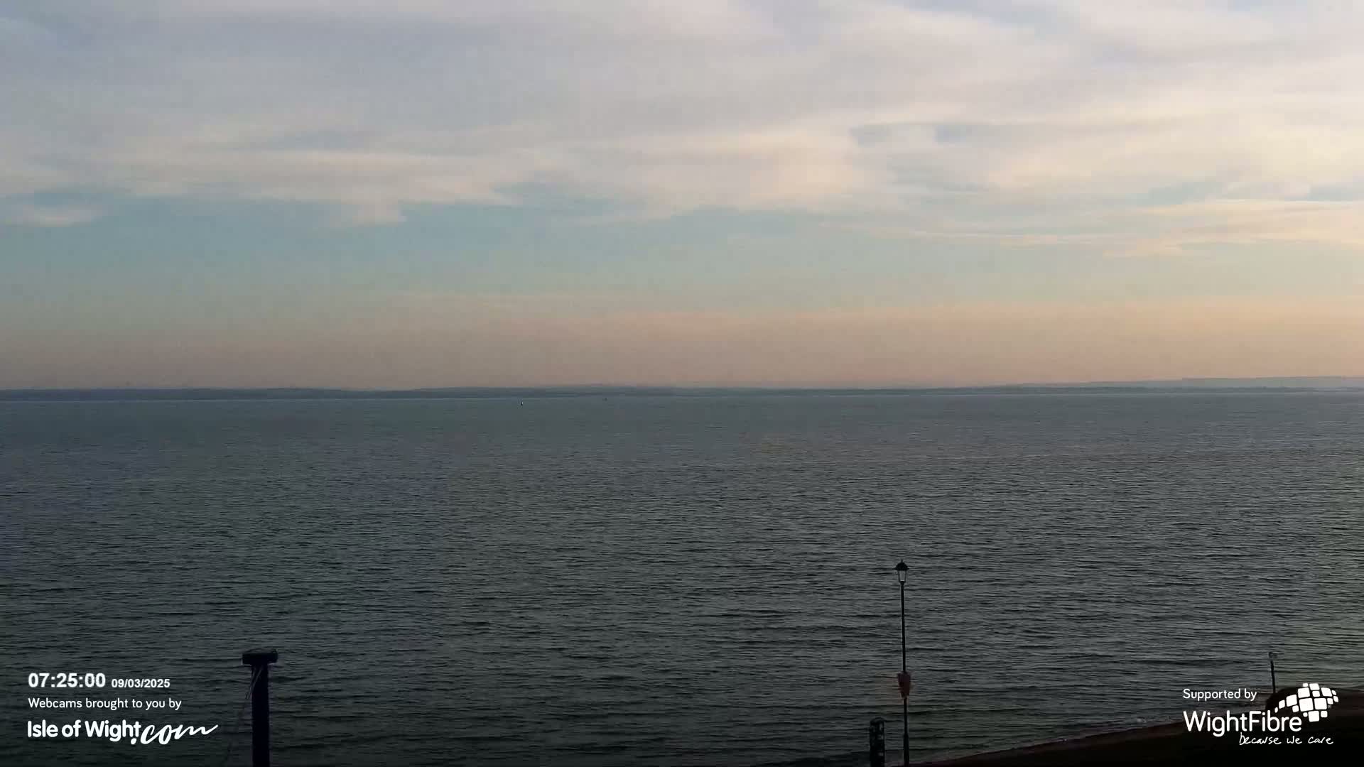 A calm body of water stretches to a hazy horizon under a lightly clouded sky.