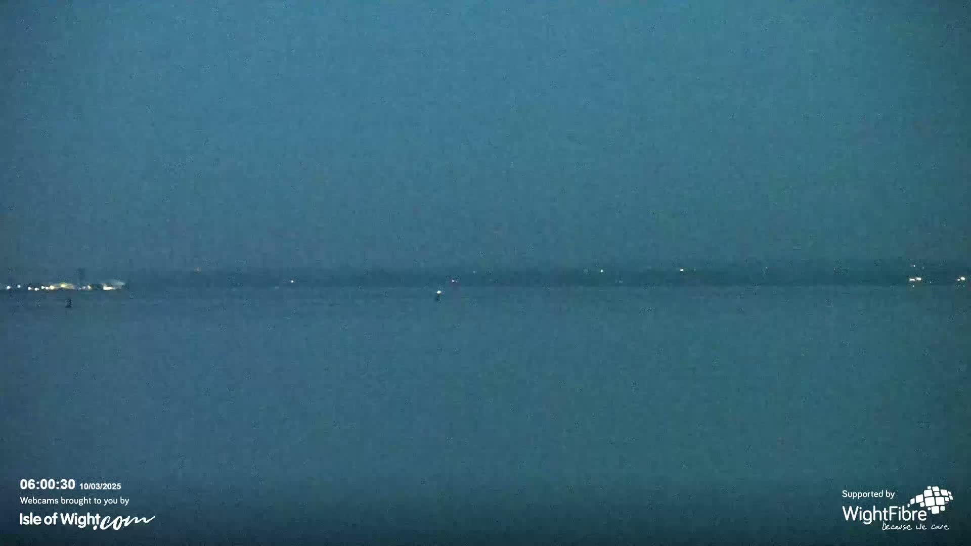 A dark, still body of water is shown at twilight, with a faintly lit distant shoreline visible on the horizon.