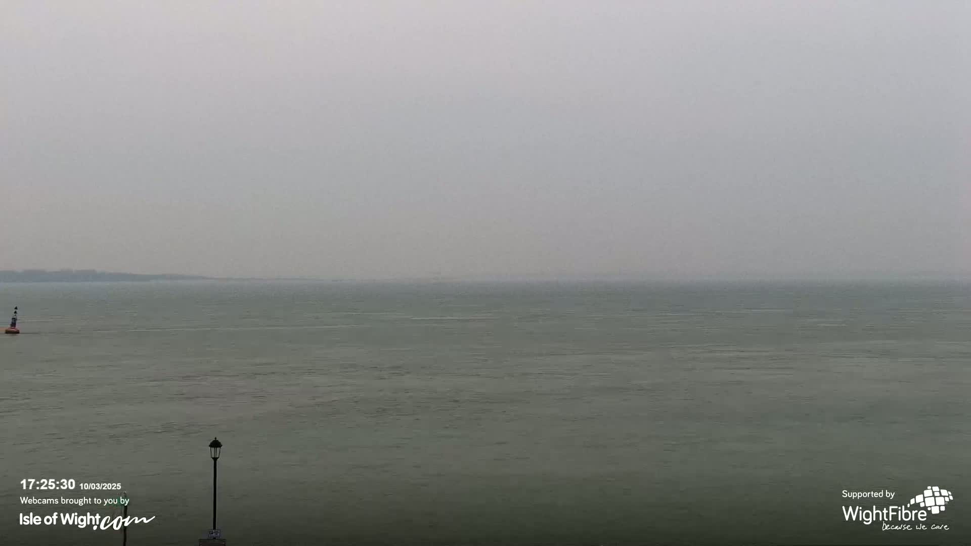 A calm, grey body of water stretches to a hazy horizon under an overcast sky.