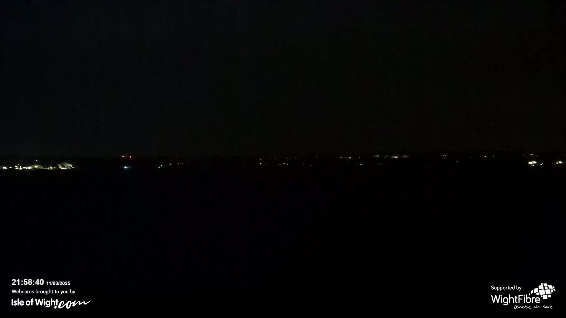A dark nighttime scene shows a distant line of faint lights across a black horizon.
