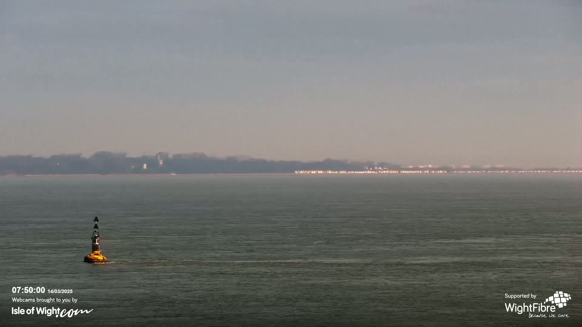 A small navigational buoy floats on calm, gray water with a distant, hazy shoreline visible in the background.
