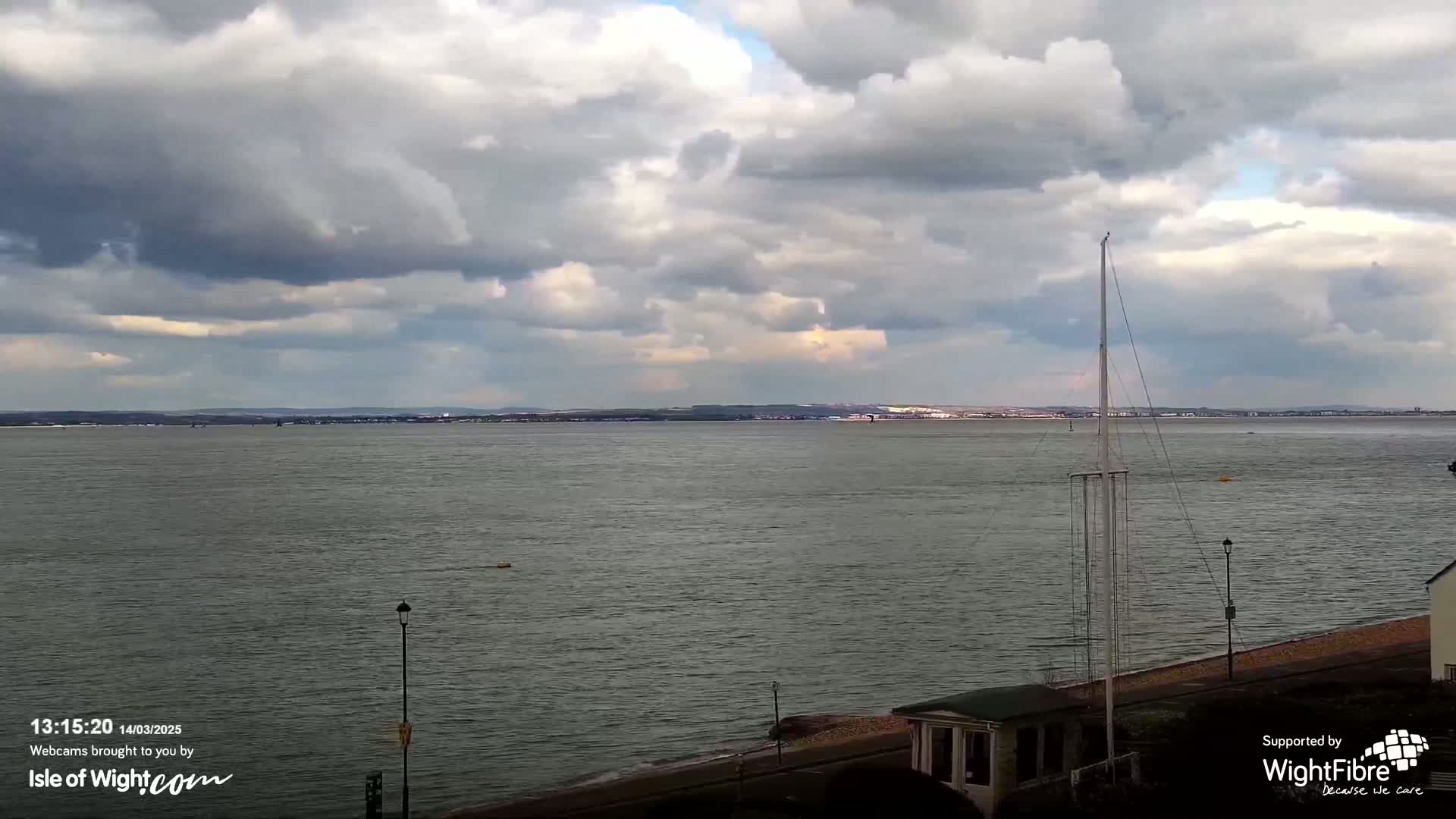 A wide, calm body of water stretches to a distant shoreline under a cloudy sky.