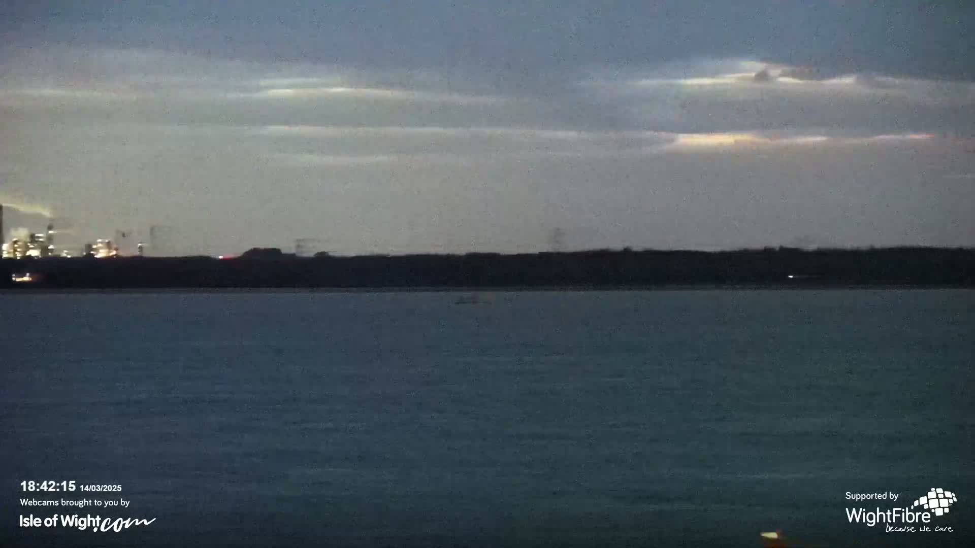 A dark body of water stretches to a distant shoreline under a twilight sky with faint, high clouds.