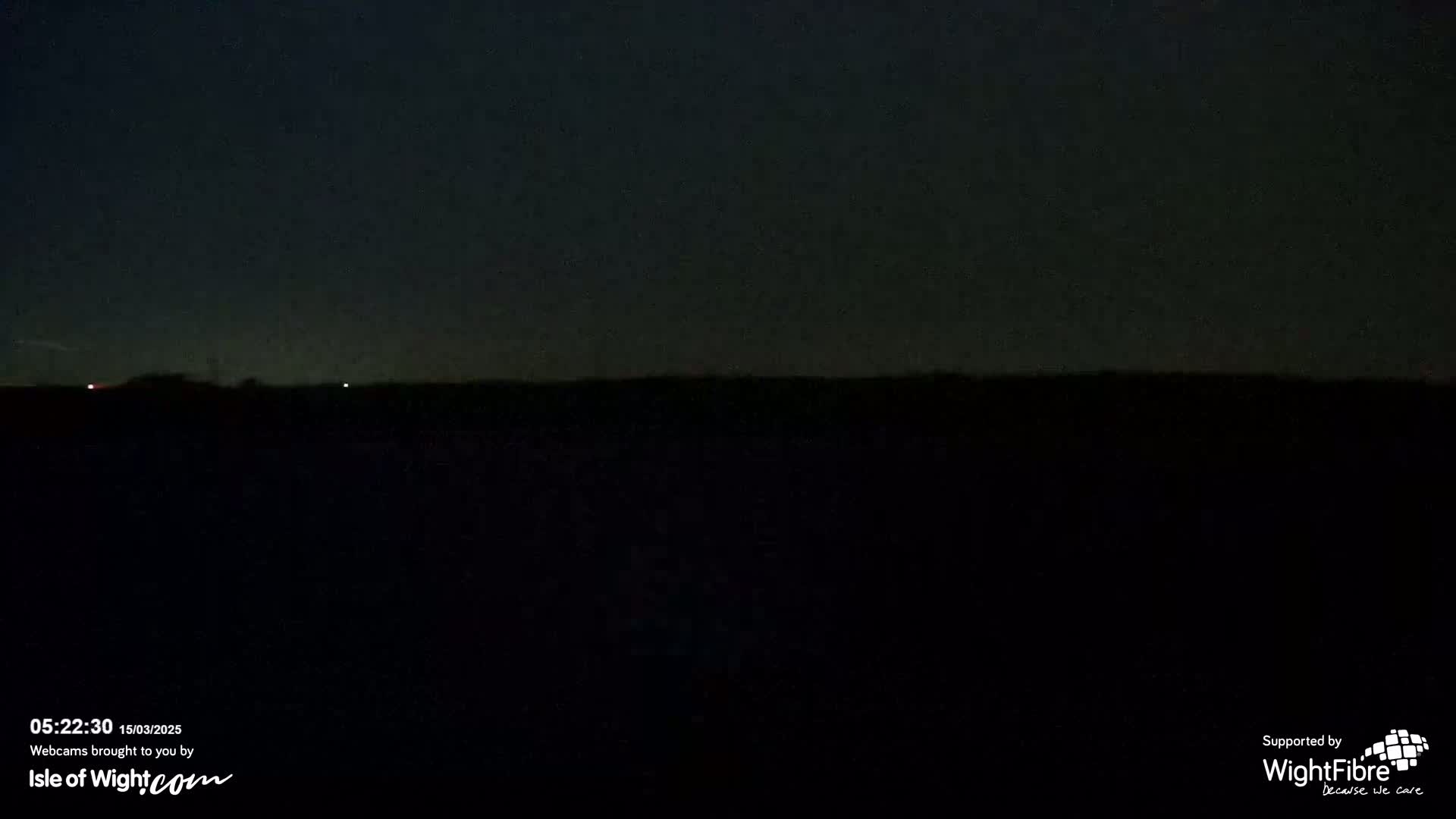 A dark, nighttime landscape is visible under a mostly clear, dark sky with two faint lights in the distance.