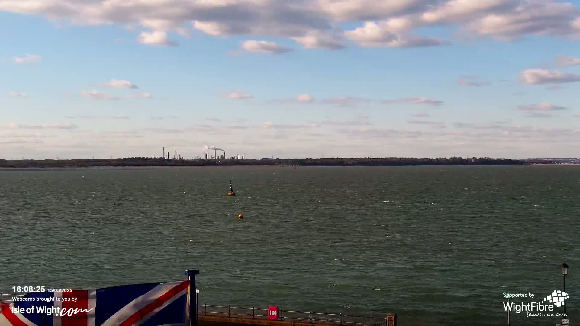 A body of water with a distant industrial coastline under a partly cloudy sky.