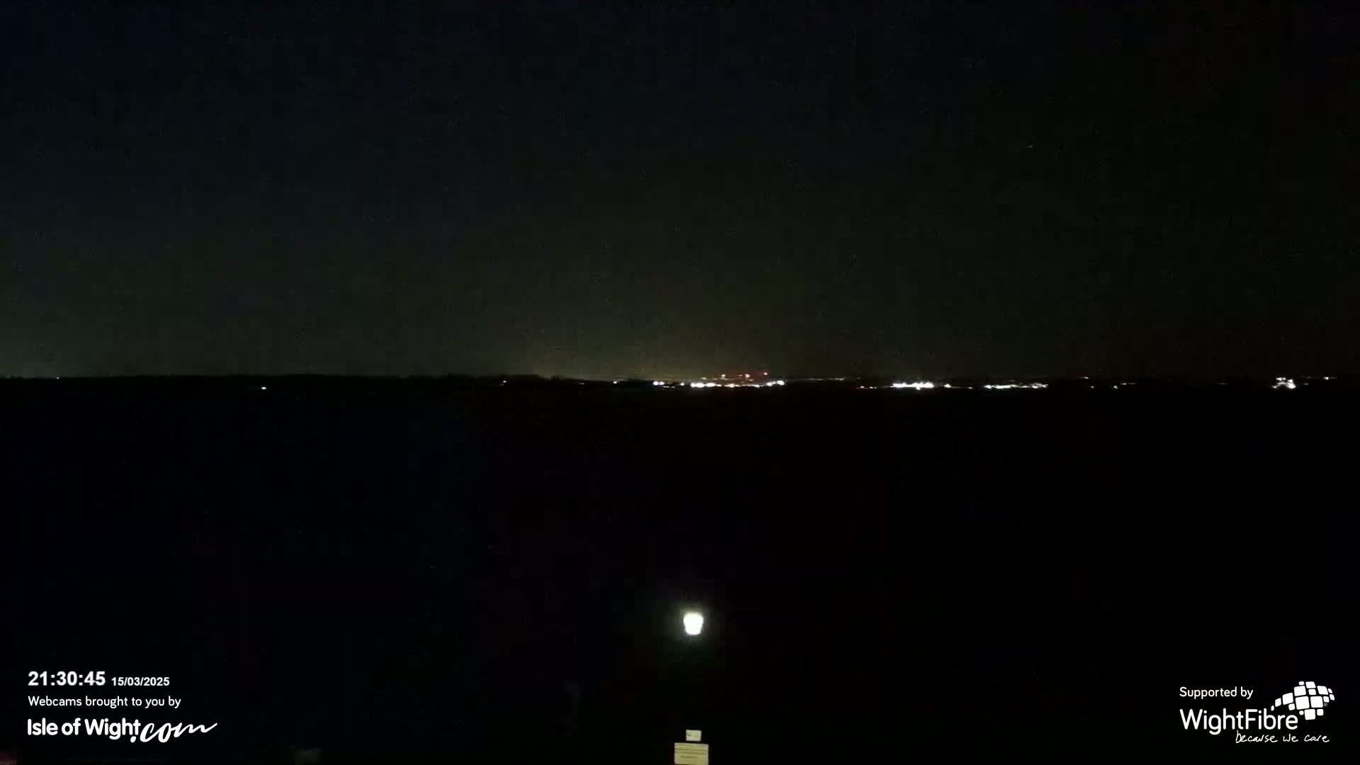A nighttime view shows a distant horizon with faint city lights under a dark, clear sky.