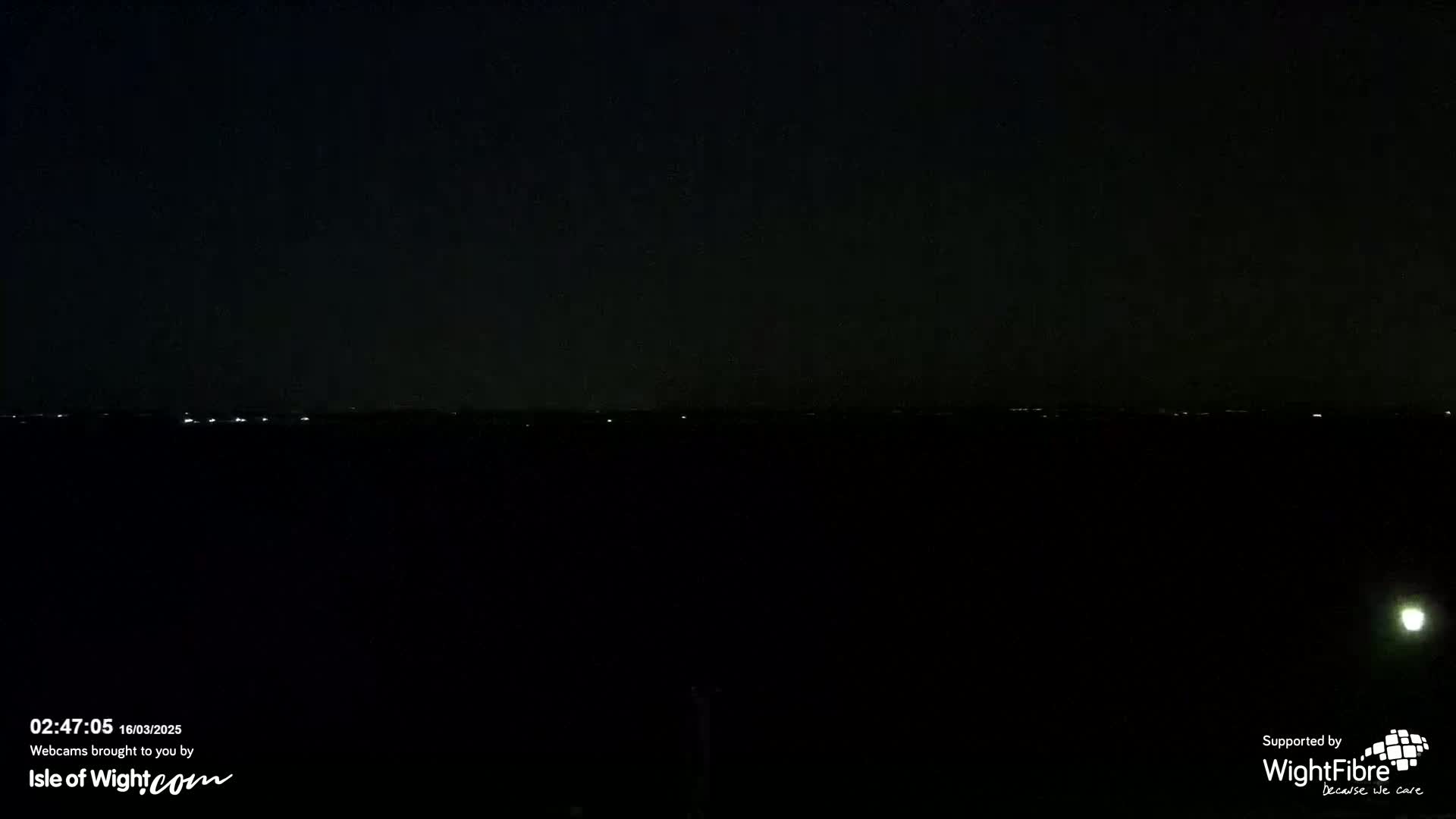 A dark, nighttime landscape shows a distant line of faint lights on the horizon.