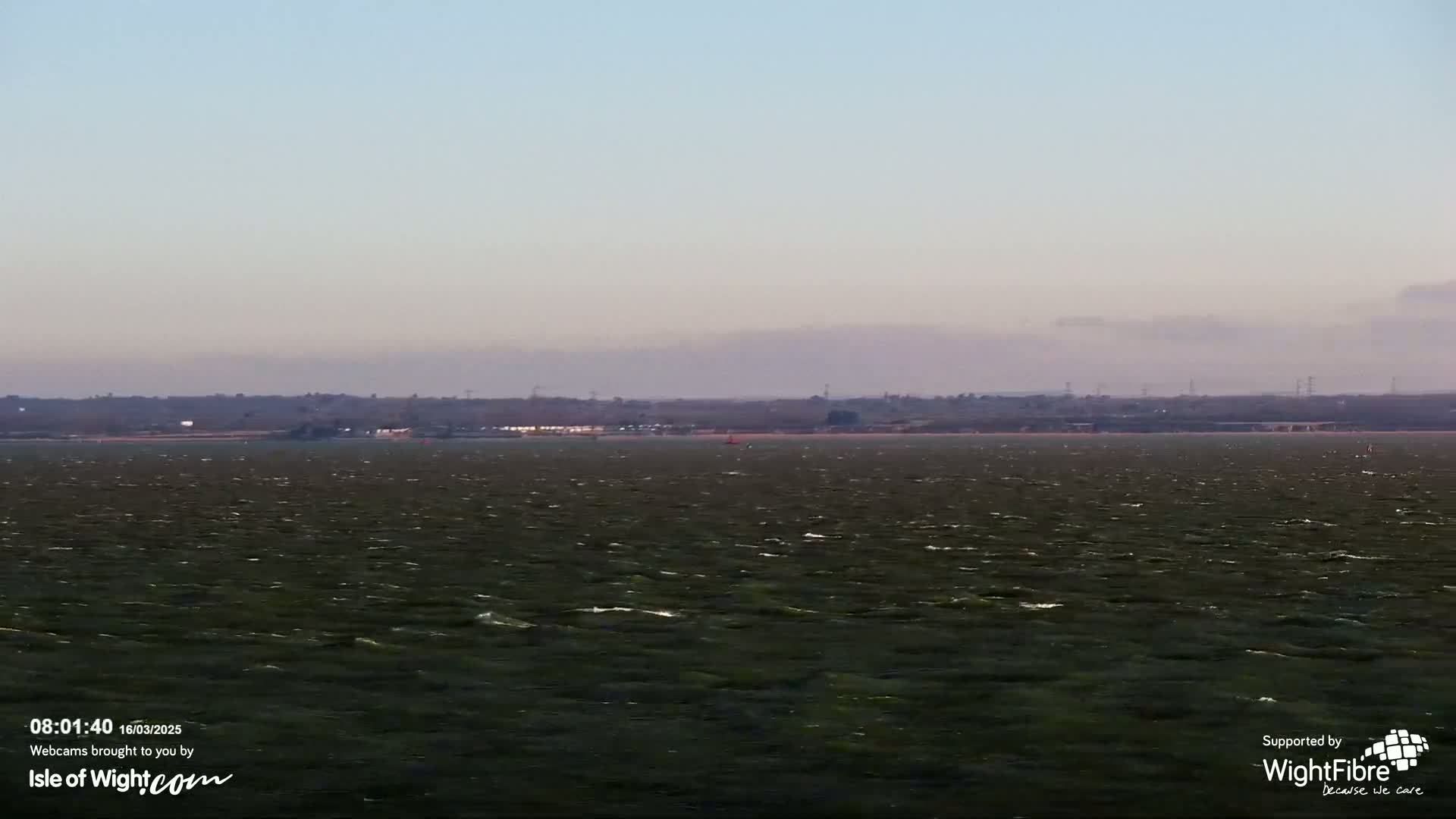 A choppy body of water stretches to a distant shoreline under a pale, hazy sky.