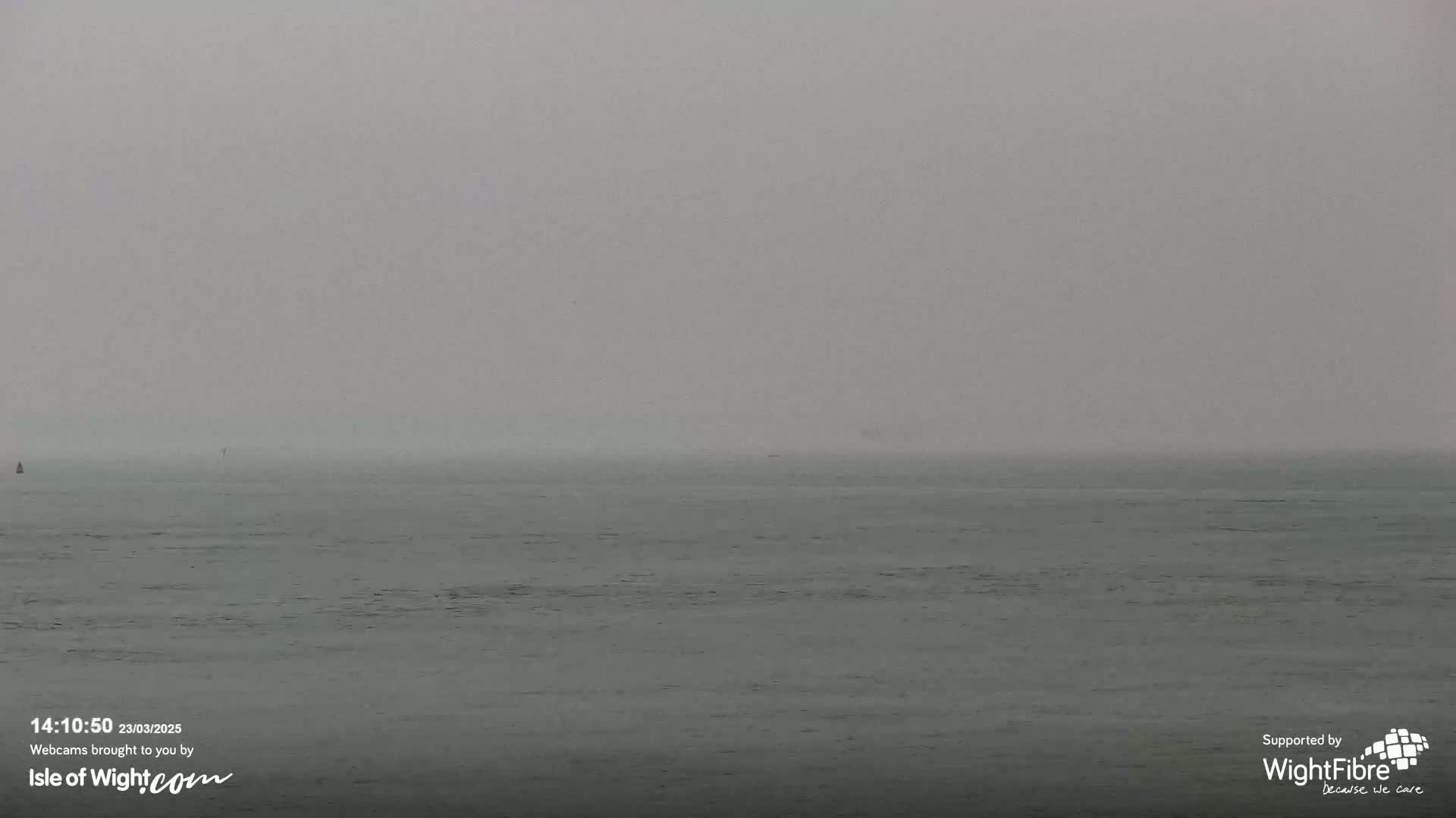A calm, gray body of water is shrouded in thick fog.