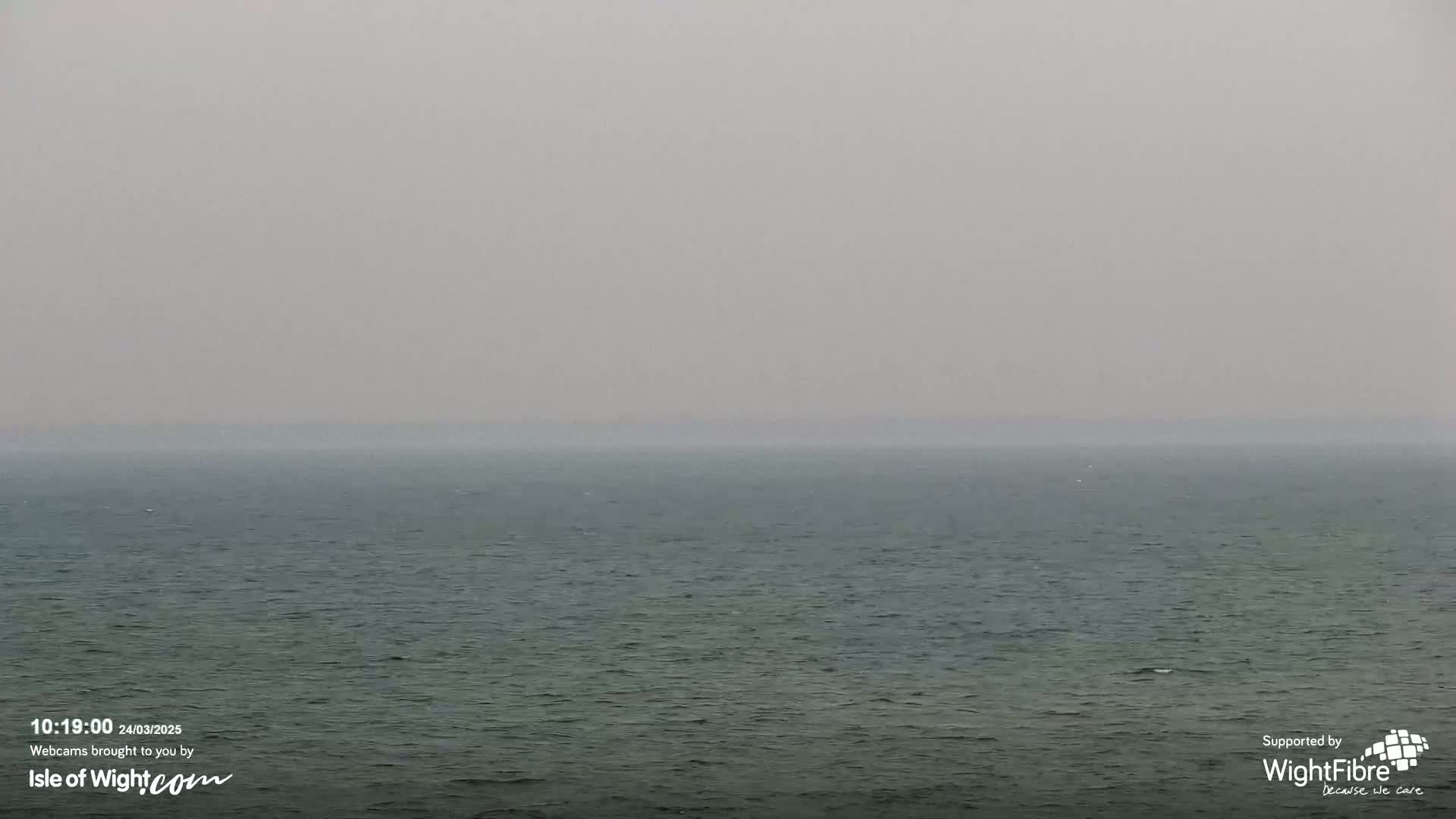 A hazy, gray sky overlooks a calm, dark-green sea.