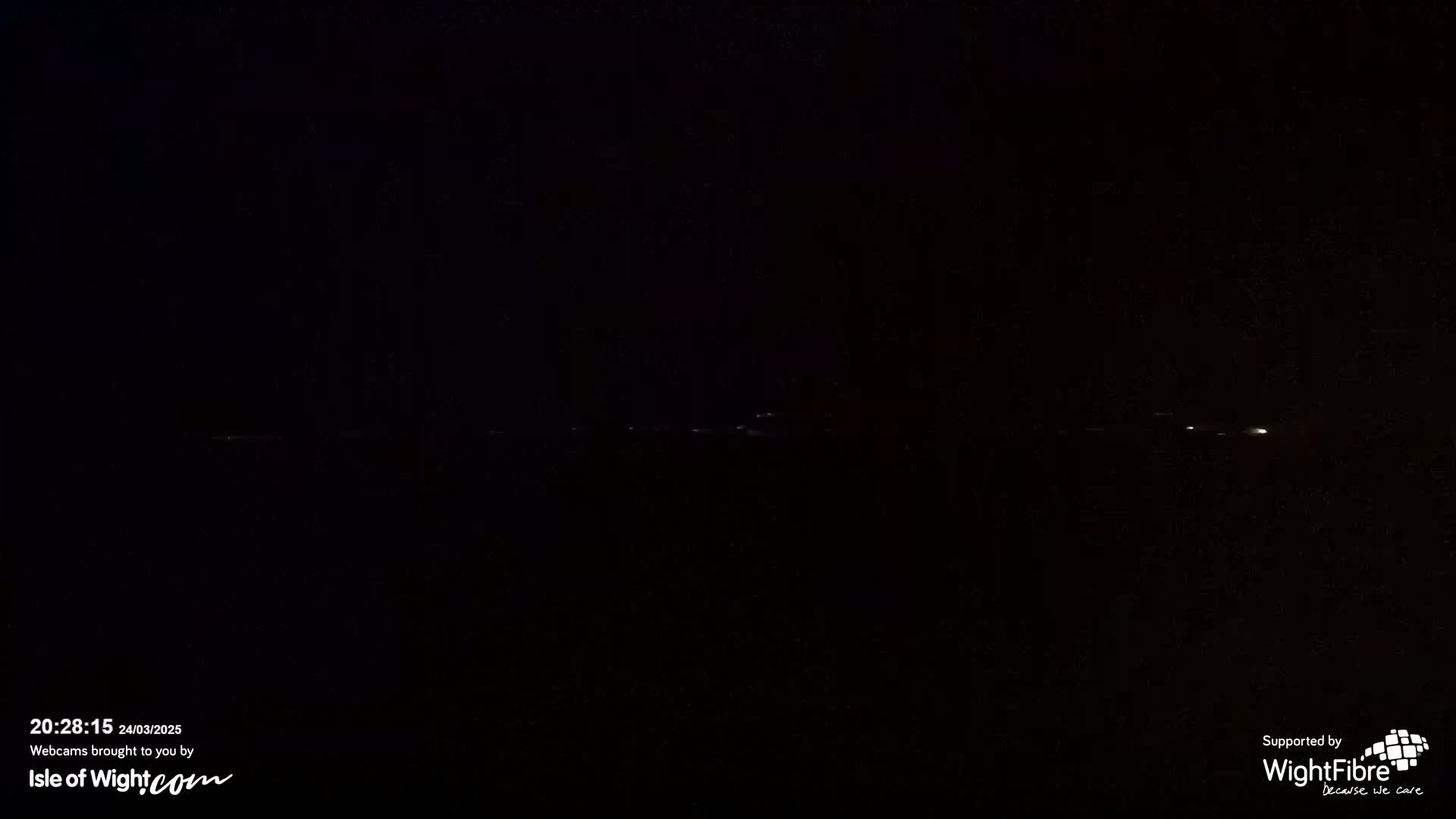A dark, nighttime scene shows a line of faint lights in the distance.
