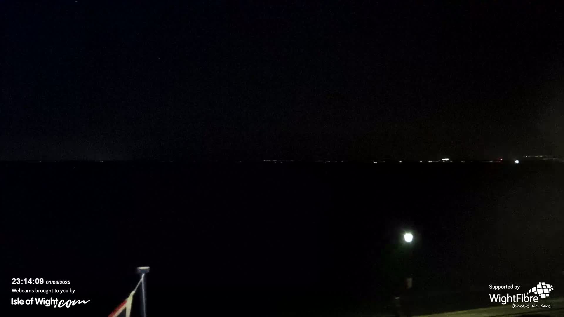 A nighttime view of a dark body of water with faintly visible lights on the horizon under a clear, starlit sky.