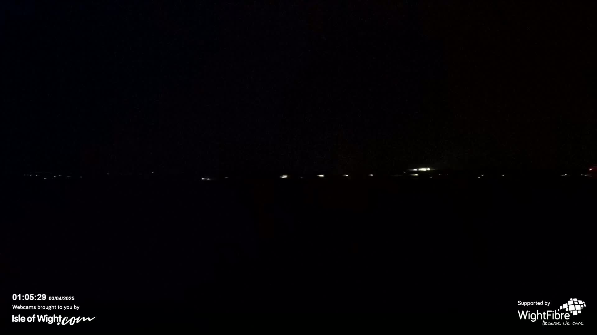 A dark, nighttime scene shows a distant line of faint lights on the horizon.