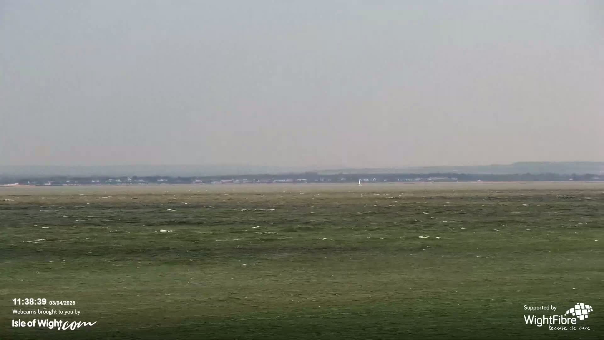 A hazy, overcast day reveals a calm body of water with a distant shoreline under a muted sky.
