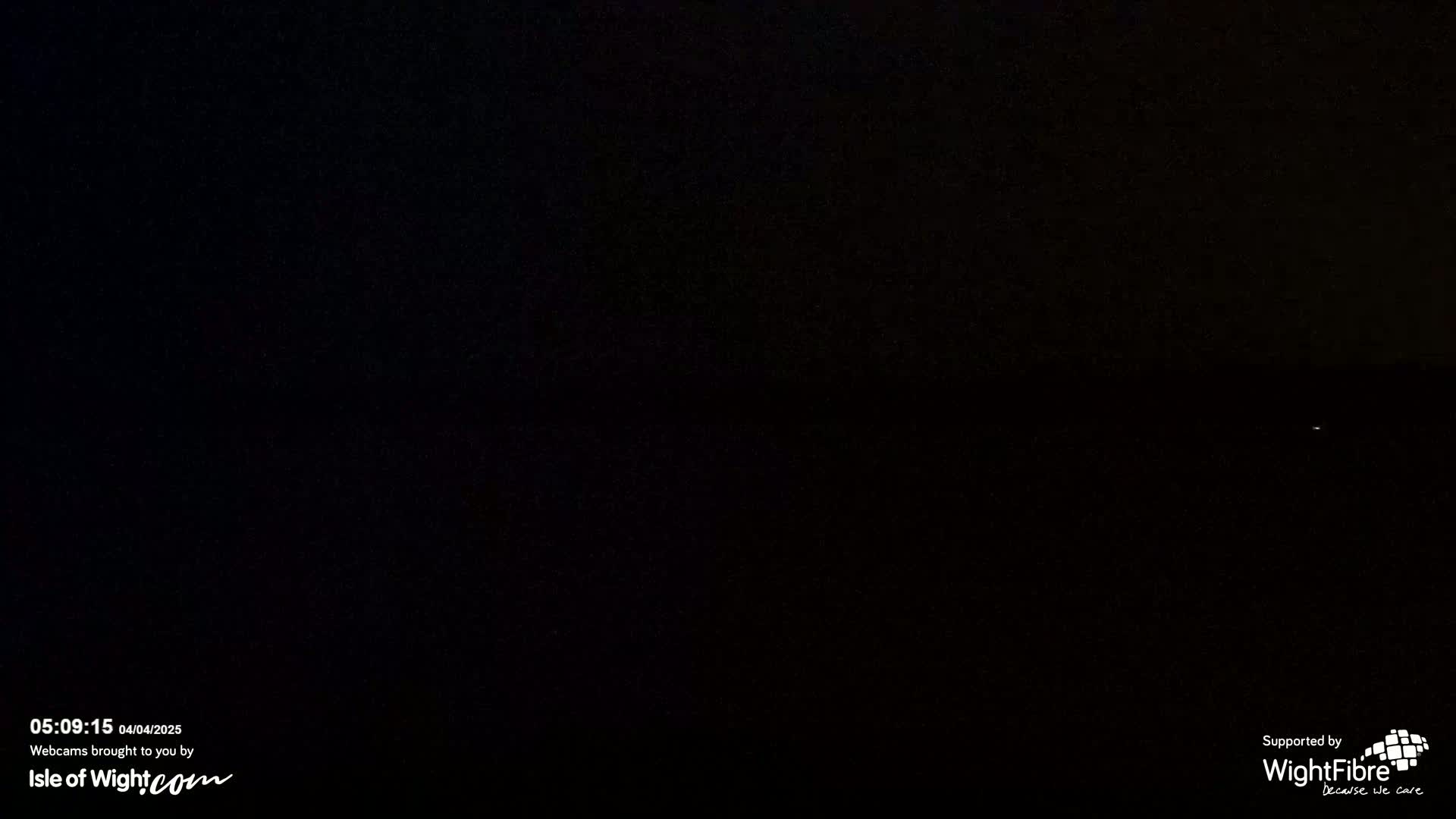 A very dark nighttime scene is visible, possibly outdoors, with a faint light source in the distance.