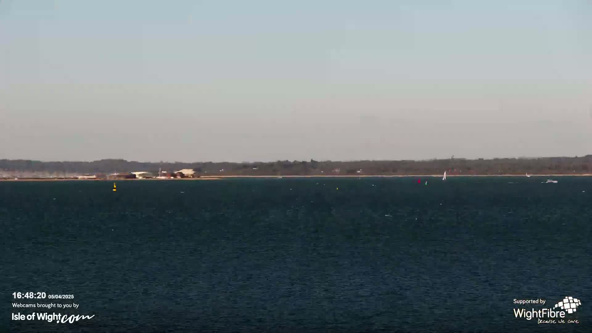 A calm, dark-blue body of water stretches to a distant shoreline under a hazy sky.