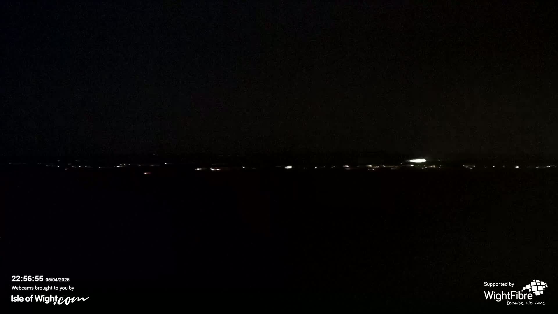 A dark nighttime scene shows a distant line of faint lights on the horizon under a clear, black sky.
