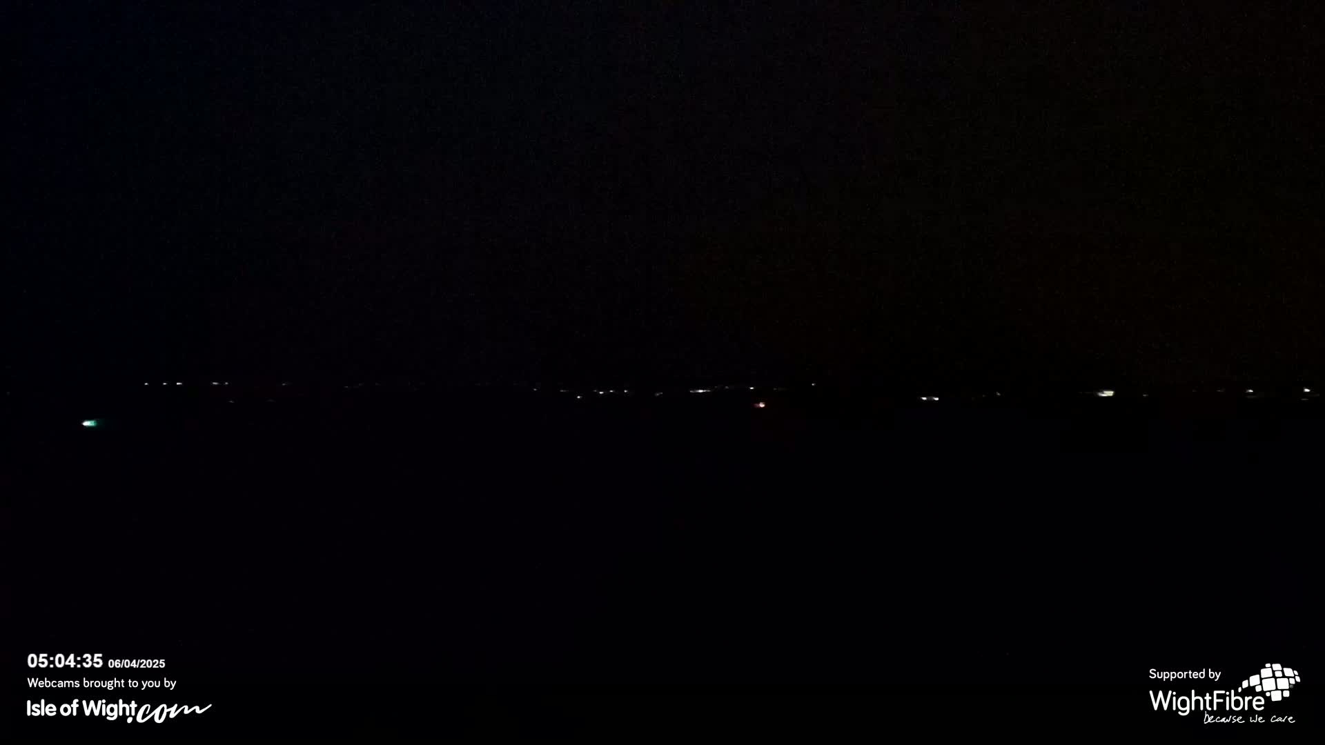 A dark, nighttime scene shows a distant line of faint lights on the horizon.