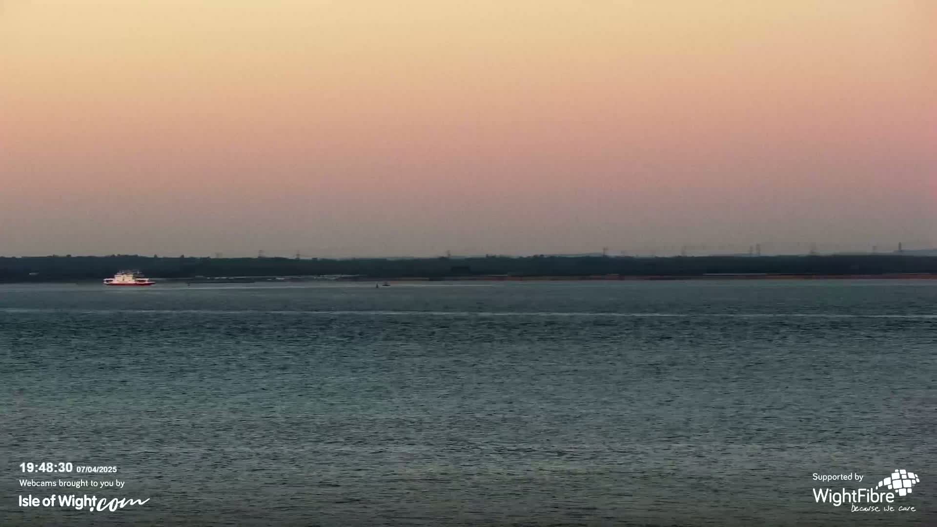 A ferry is on calm water under a pale pink sky at dusk.