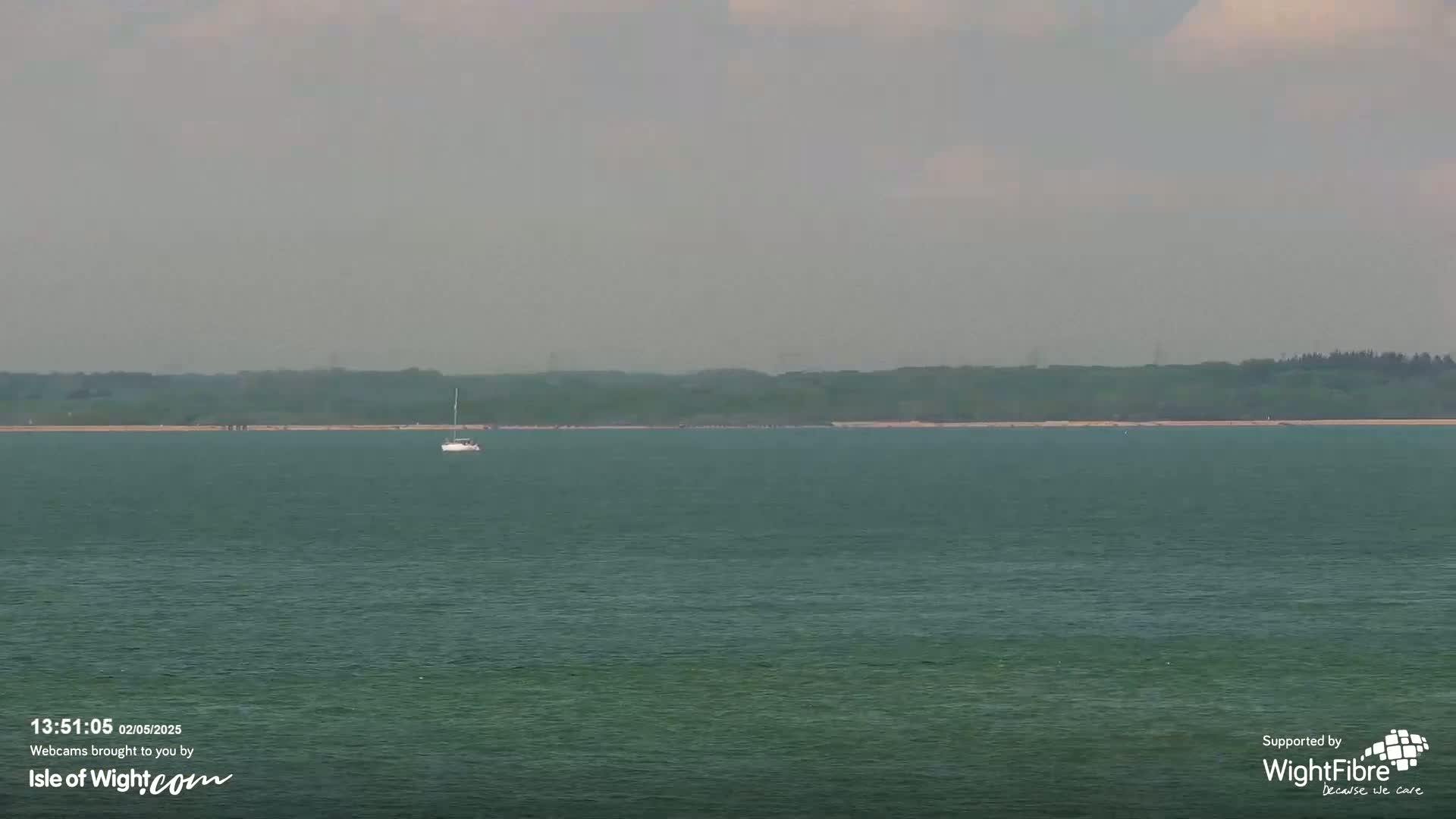 A sailboat is visible on a calm, somewhat hazy body of water with a treeline in the distance.