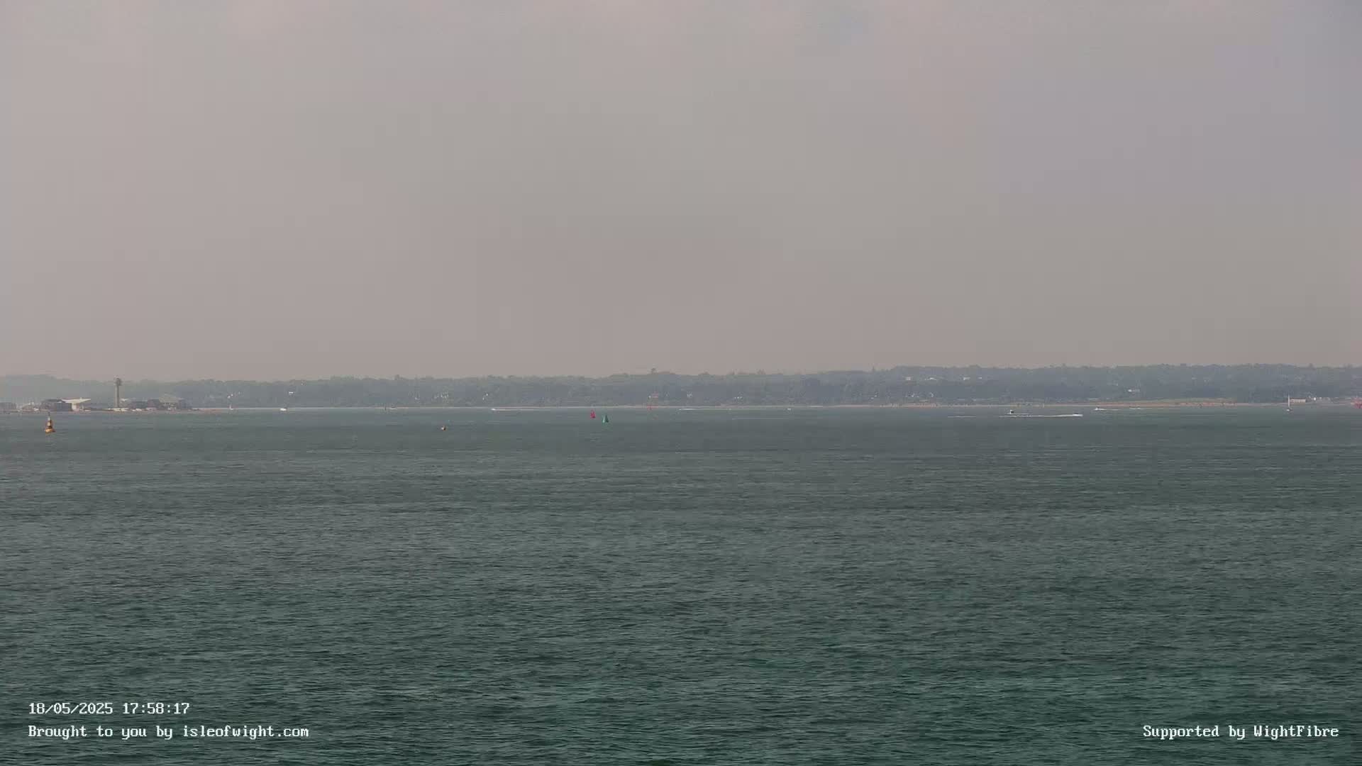 A hazy, calm body of water shows a distant shoreline with a few small boats.